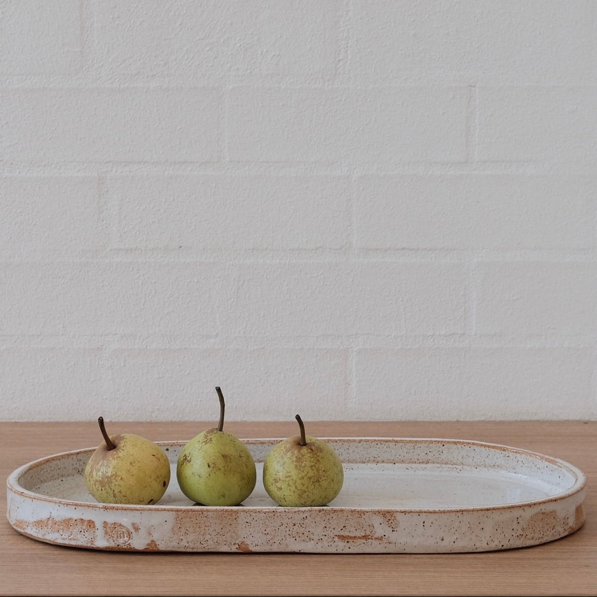 Three pears on an oval ceramic tray against a white textured wall.
