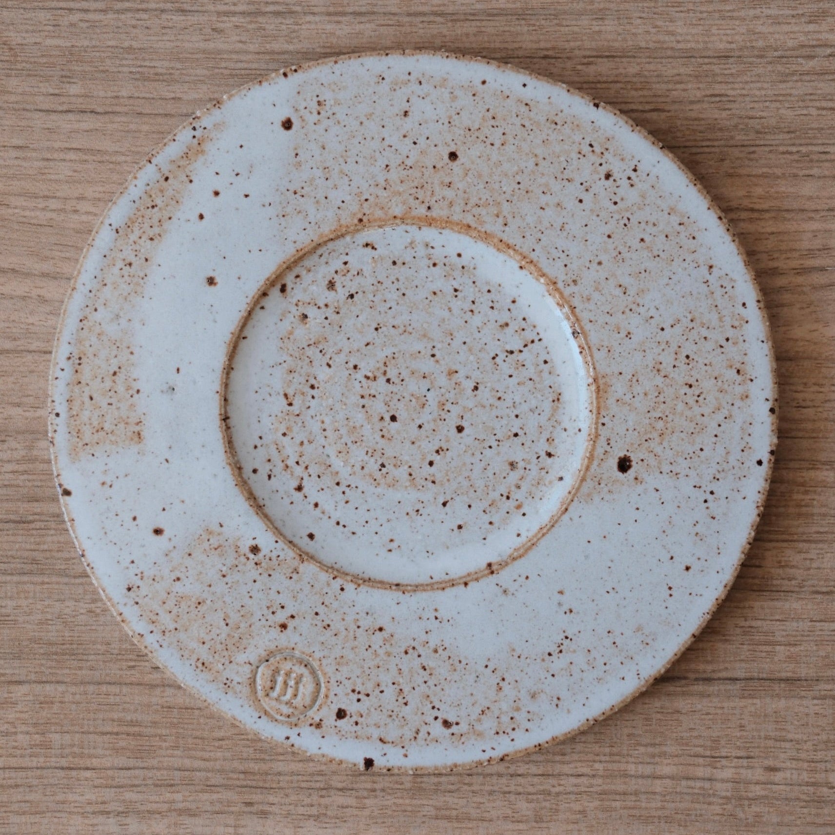 Speckled warm white ceramic coaster or drip trap on a wooden surface