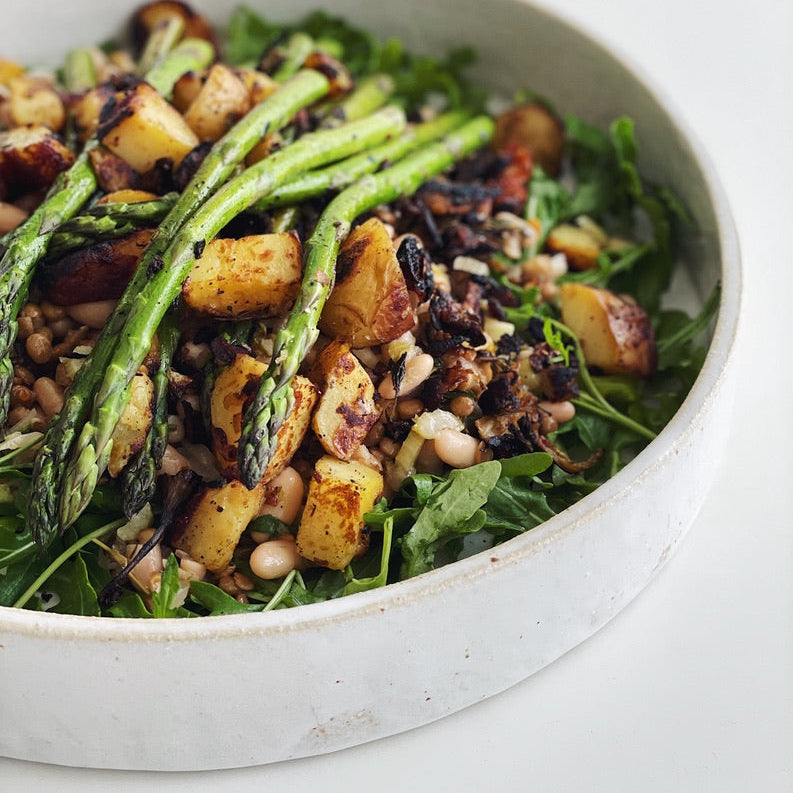 Salad with asparagus, potatoes, and greens in a white bowl on a light background