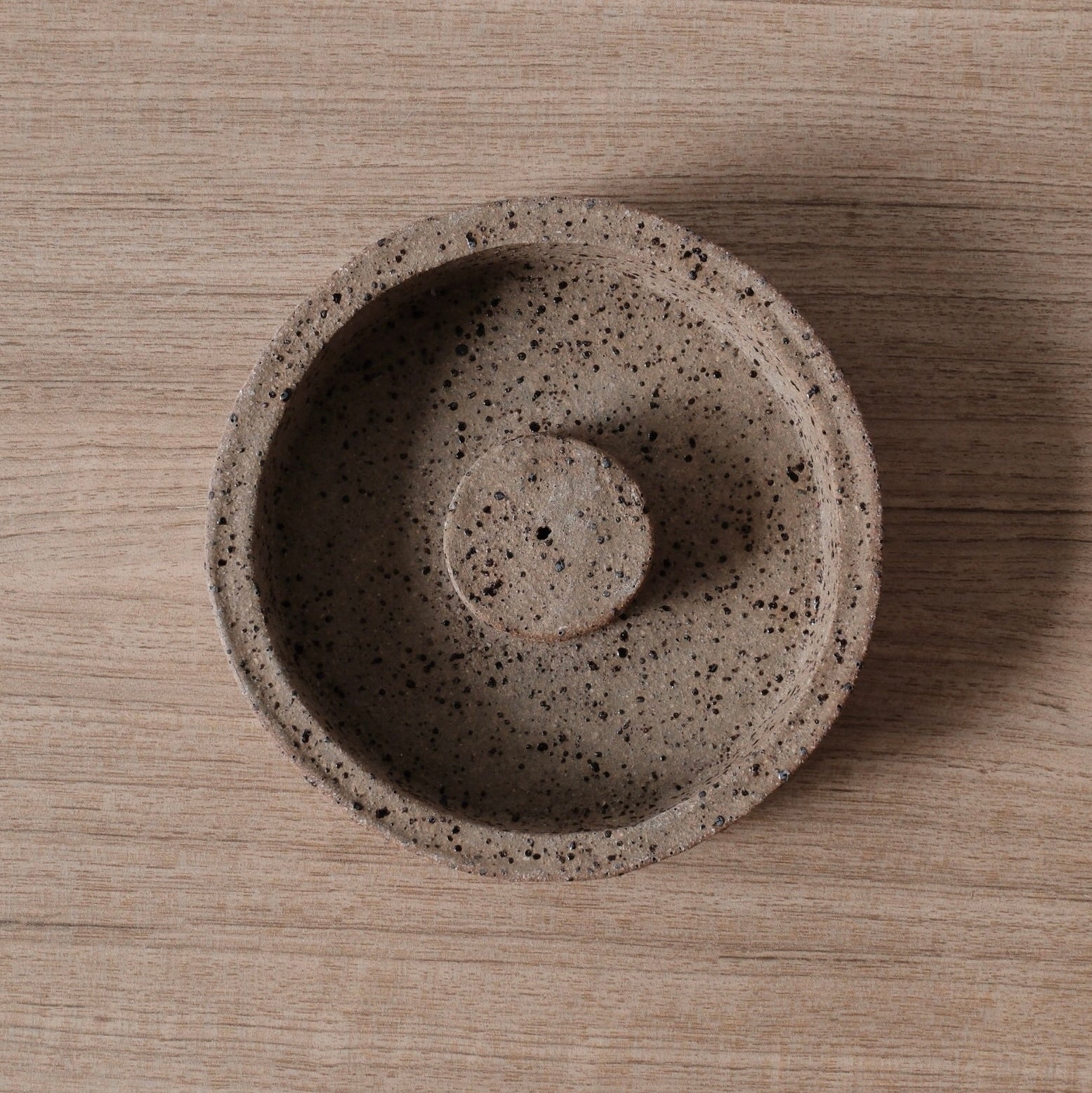 A birds-eye-view of a ceramic incense holder with warm brown textured surface on a wooden bench