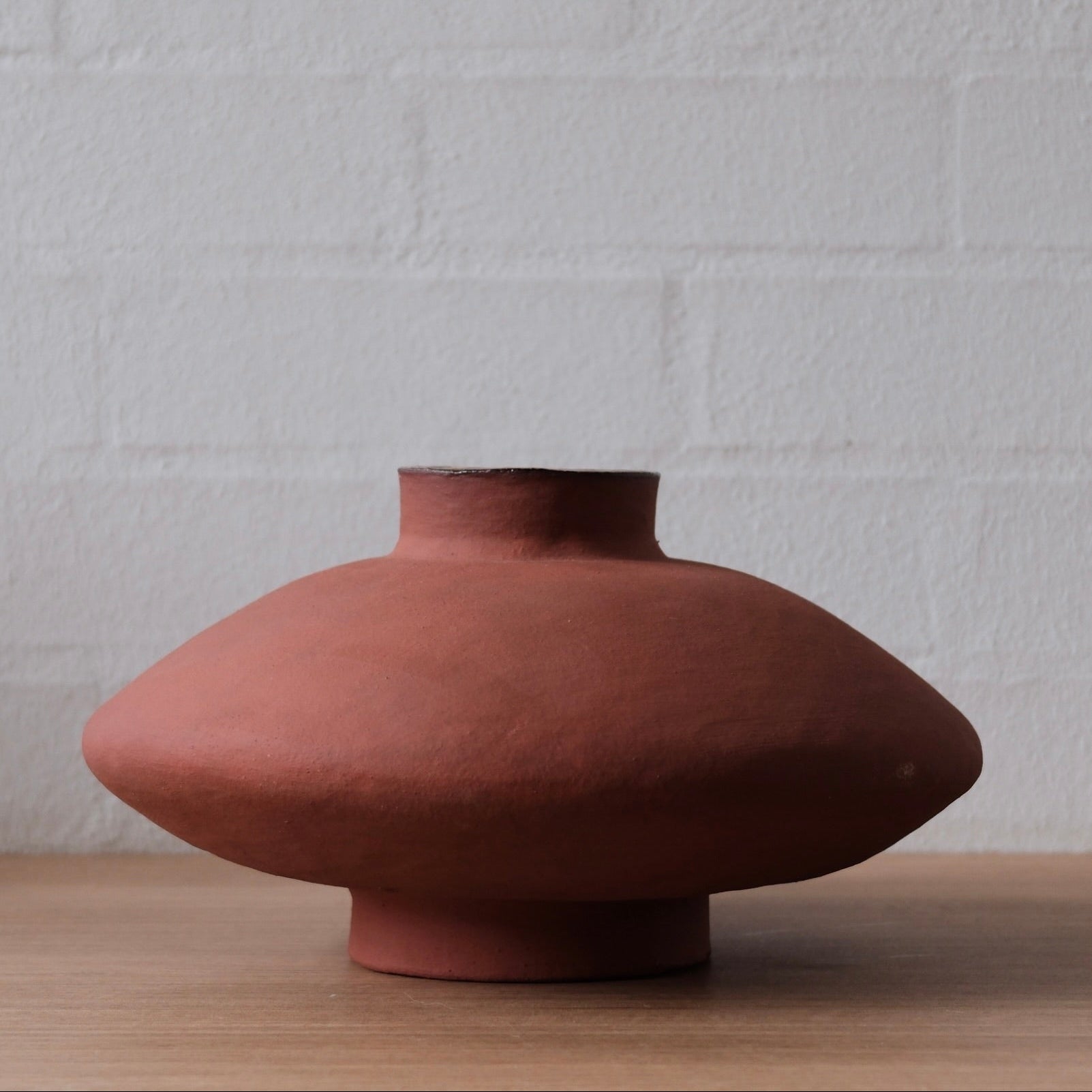 Terracotta vessel on a wooden surface with a white textured wall background