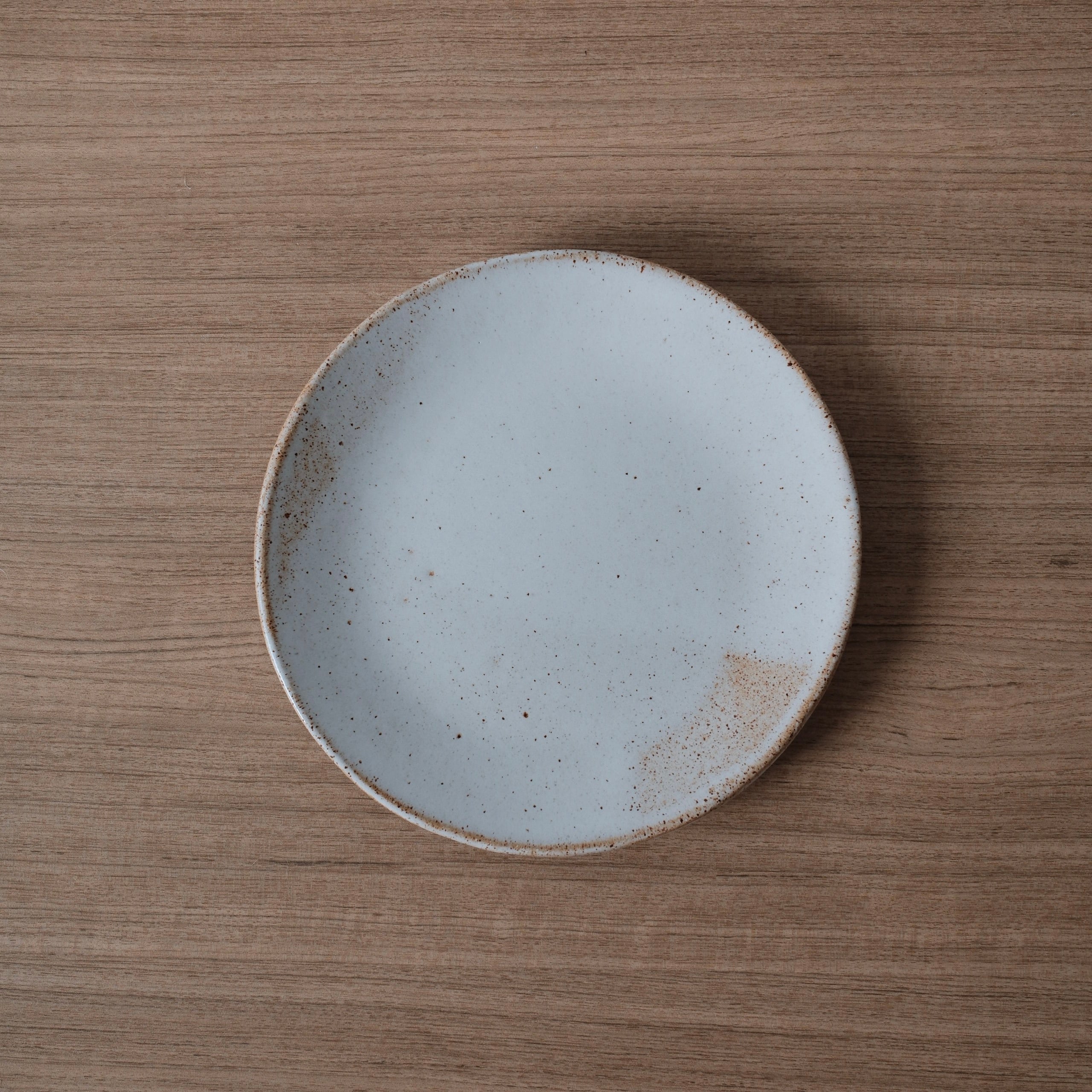Round white ceramic lunch plate with a slightly speckled finish and golden highlights on a wooden surface