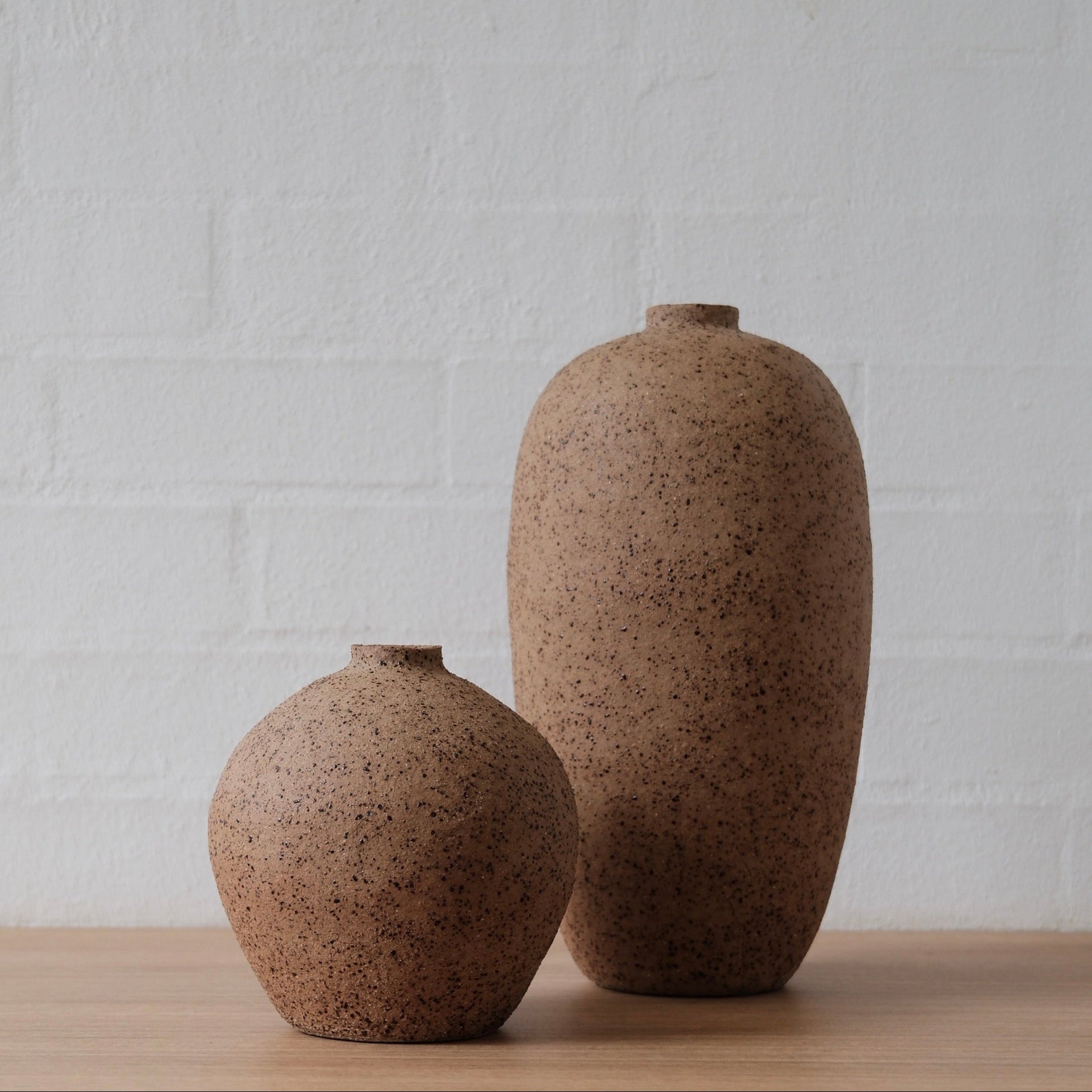 Two brown ceramic vessels on a wooden surface with a white textured wall background.