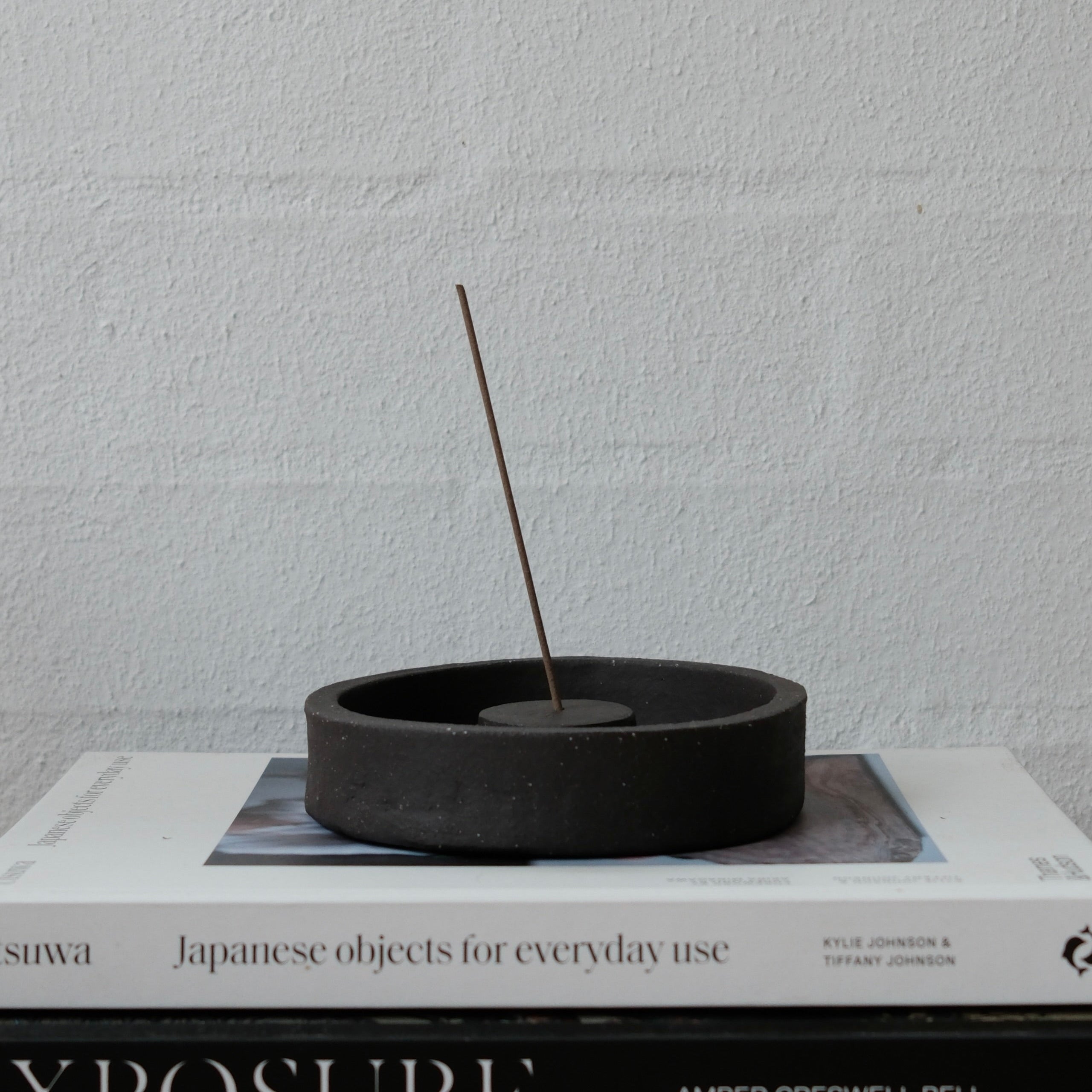 Black ceramic incense holder with a single incense stick on top of a book.