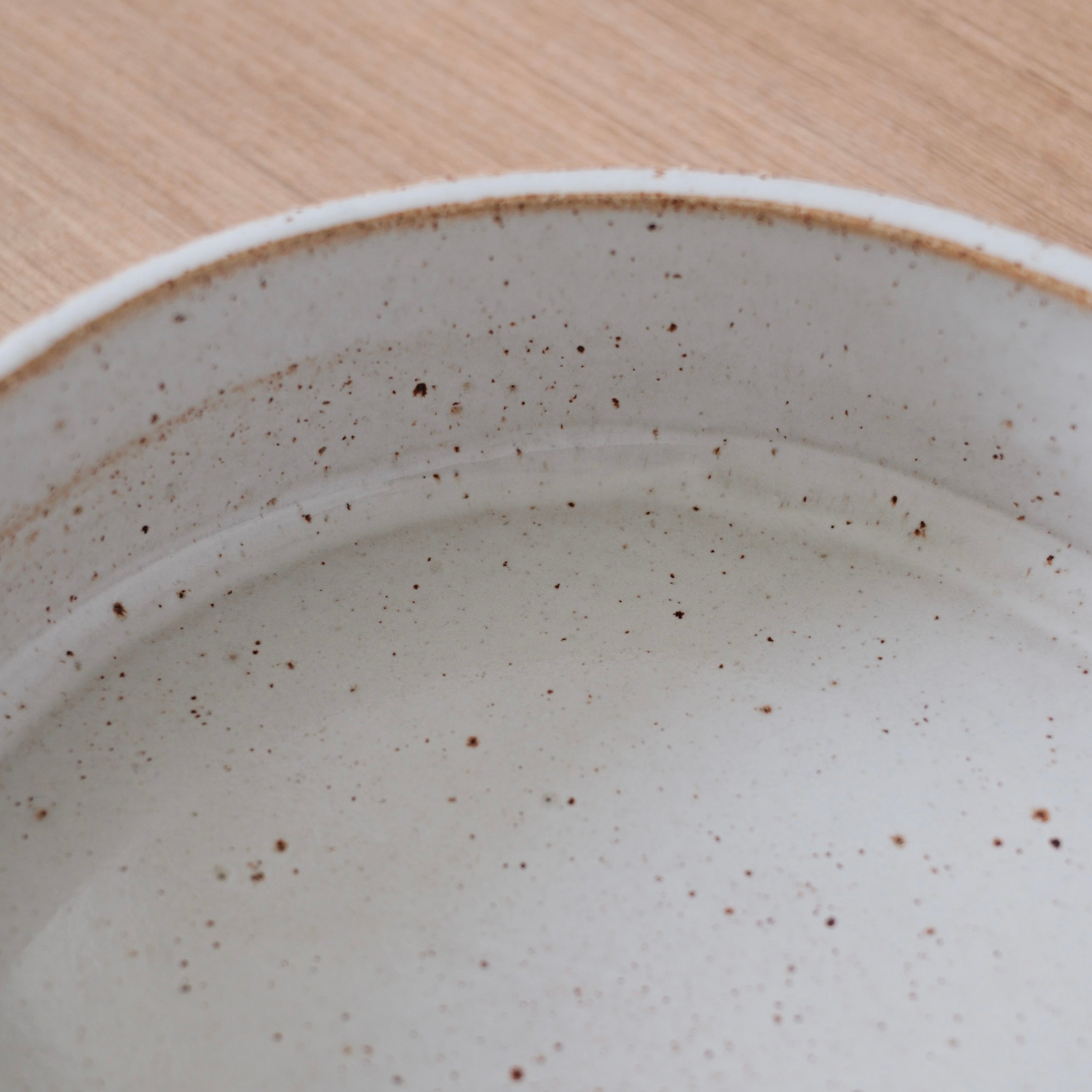 Close up of the inside of a white ceramic bowl with slightly speckled golden finish on a wooden surface.