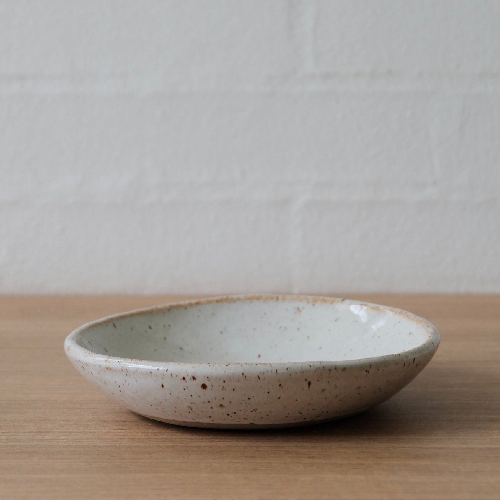 White ceramic bowl with golden flecks on a wooden surface with a white background