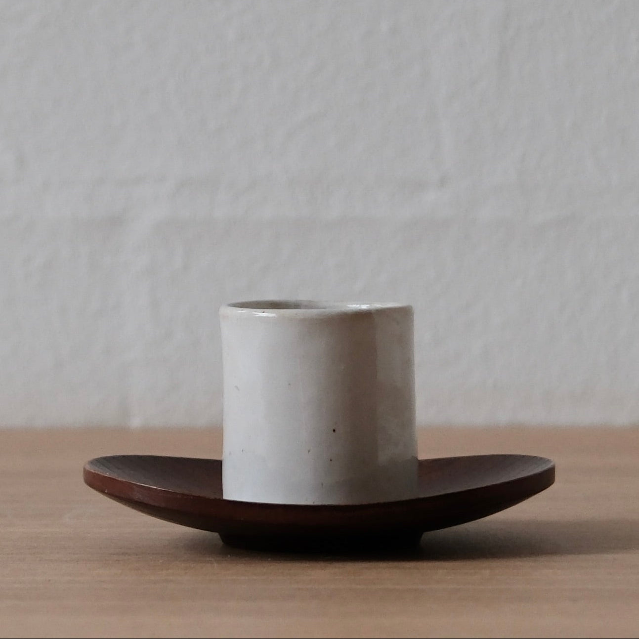 Ceramic espresso cup on a wooden saucer against a plain background