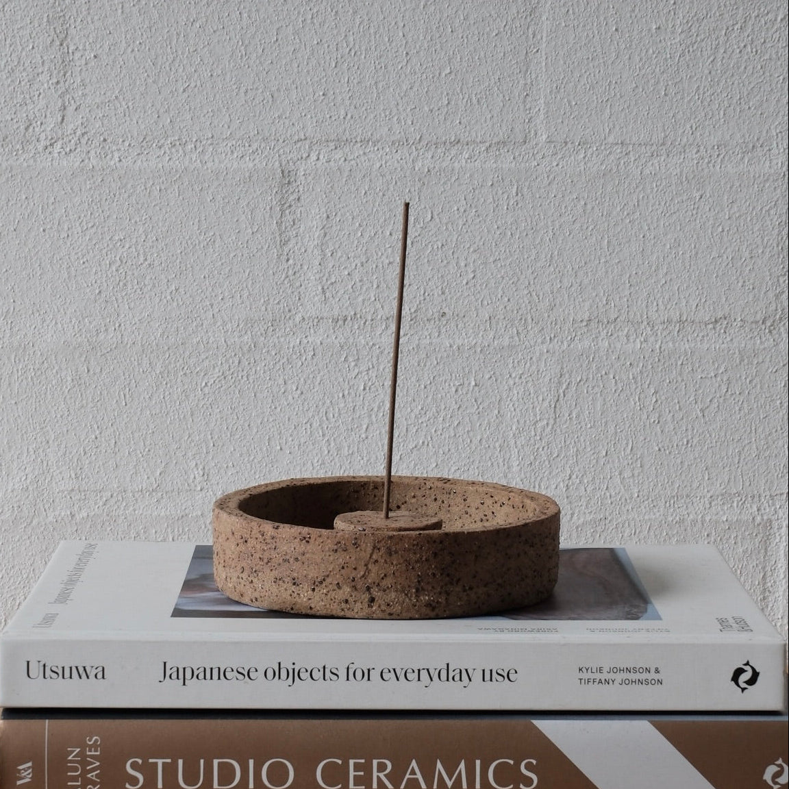 Ceramic incense burner on top of two books with a plain wall background