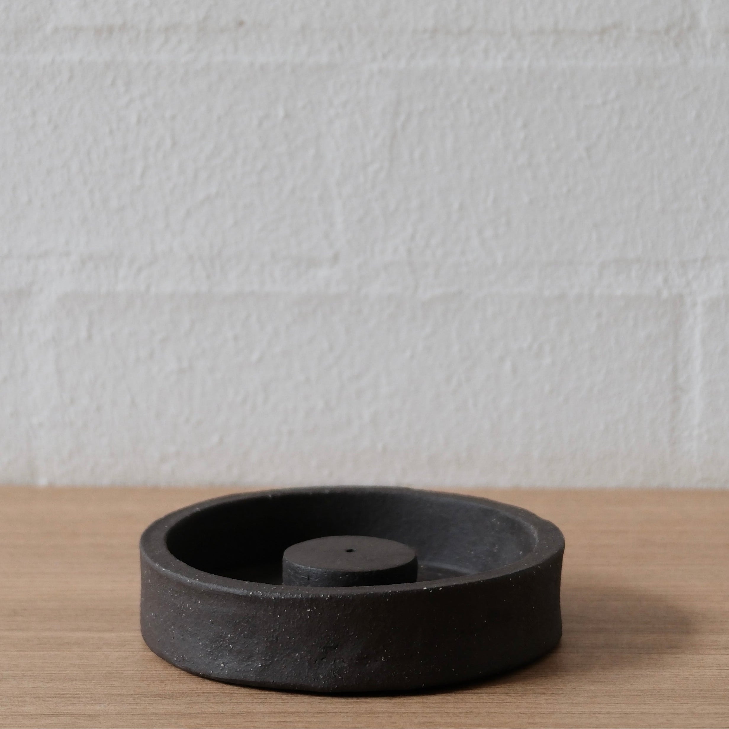 Black ceramic incense holder on a wooden surface with a white textured wall background