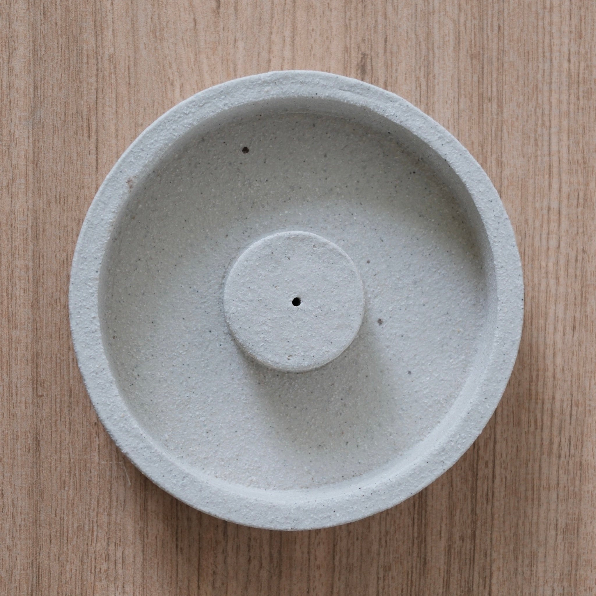 Top-down-view of round, textured, white ceramic incense holder on a wooden surface