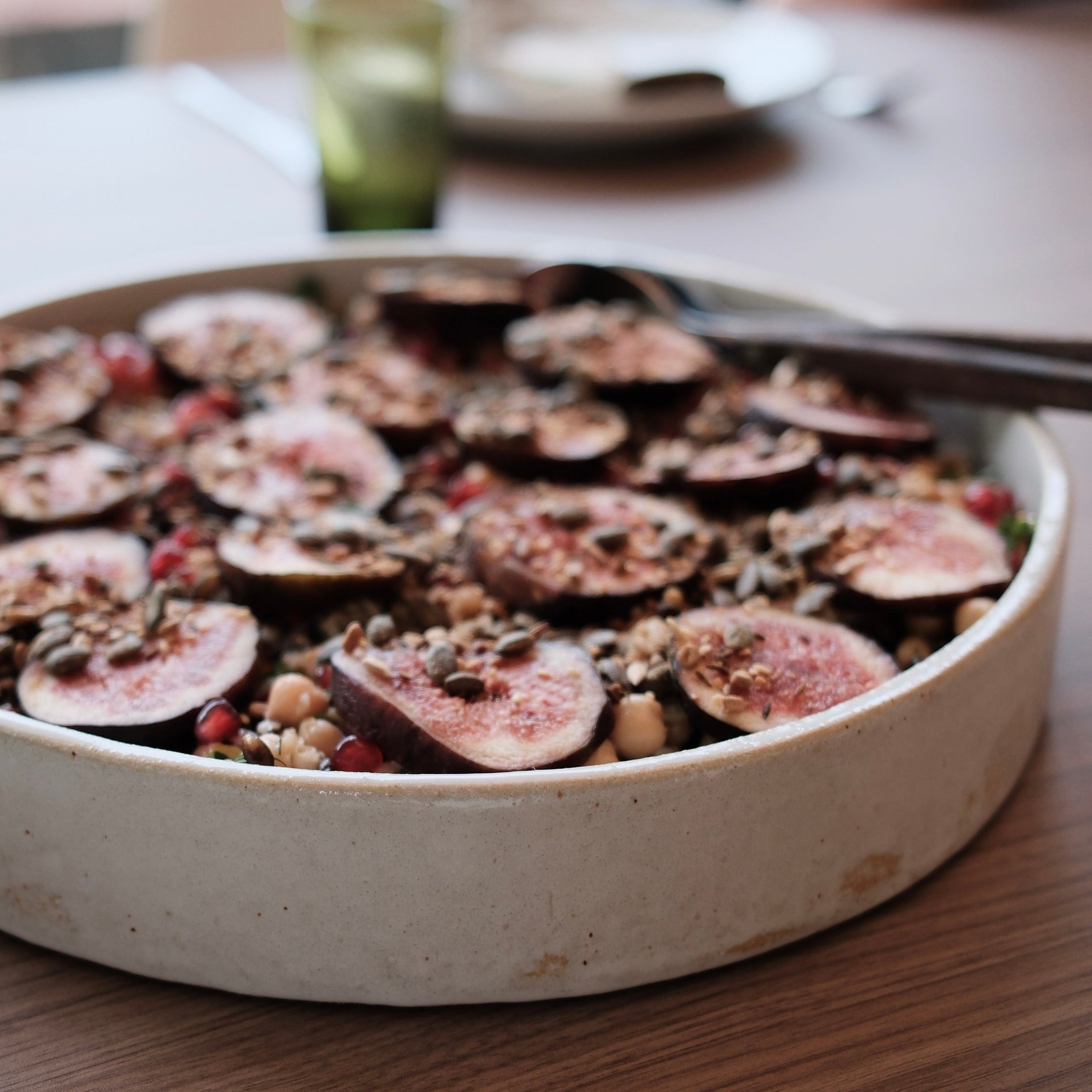 Salad garnished with sliced figs and seeds in a low stacking dish on a wooden table