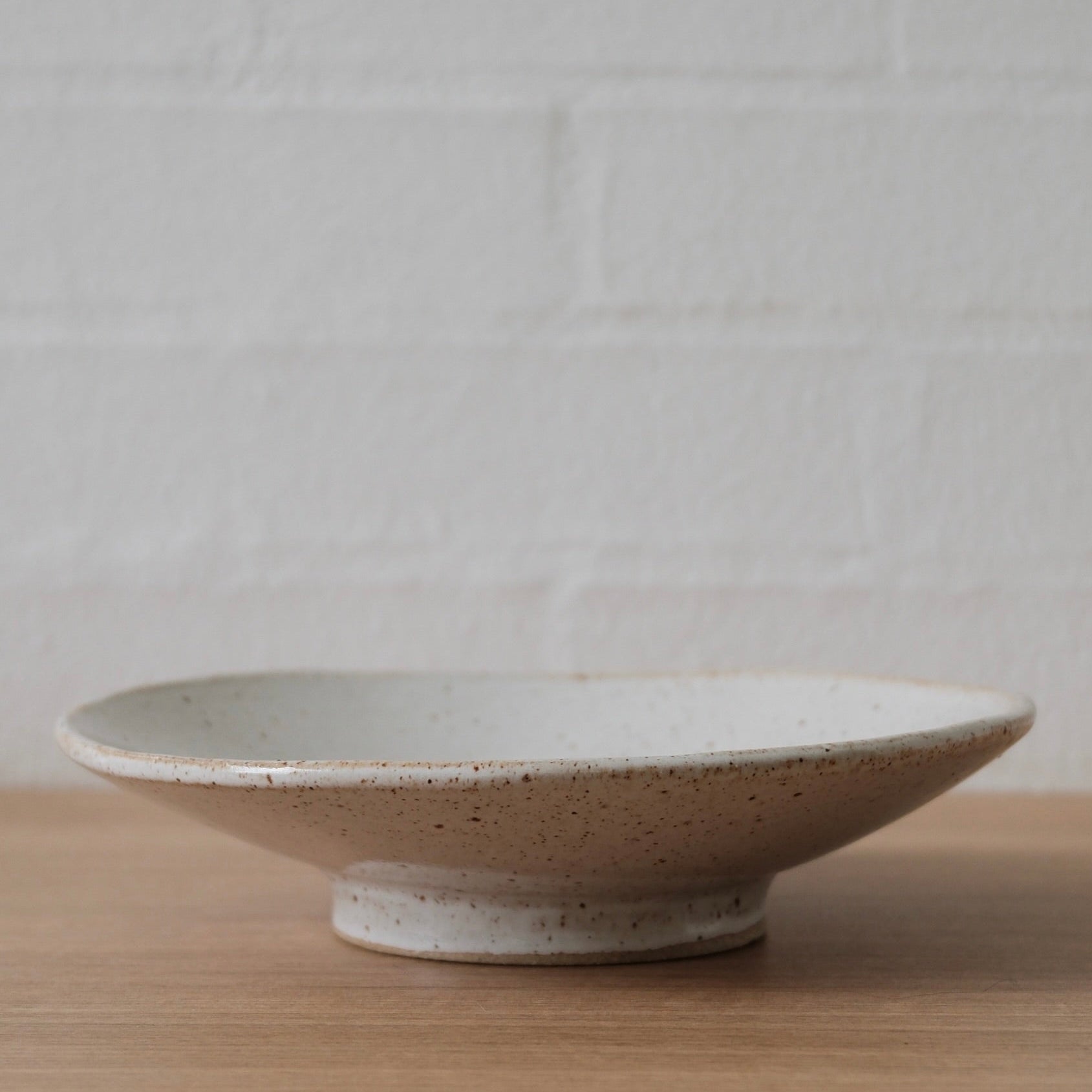 White ceramic bowl on a wooden surface with a white textured wall background
