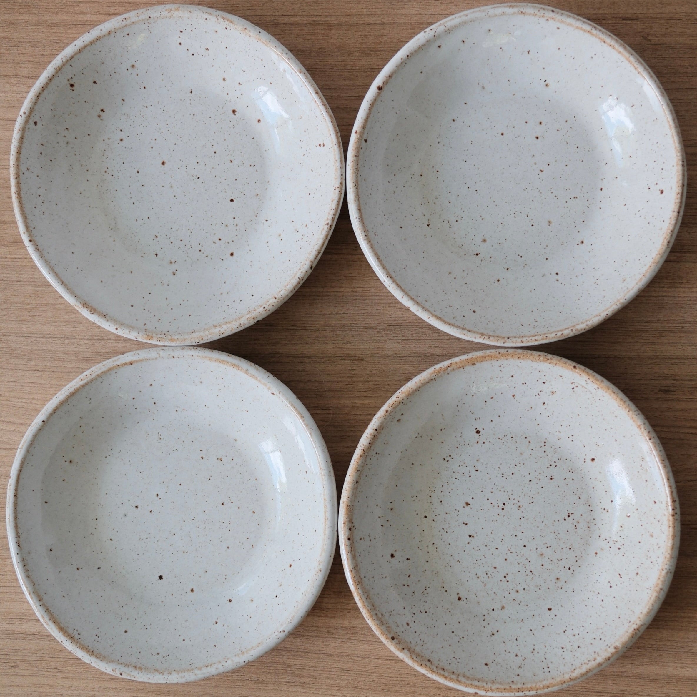 Birds-eye-view of four white ceramic bowls with speckles on a wooden surface