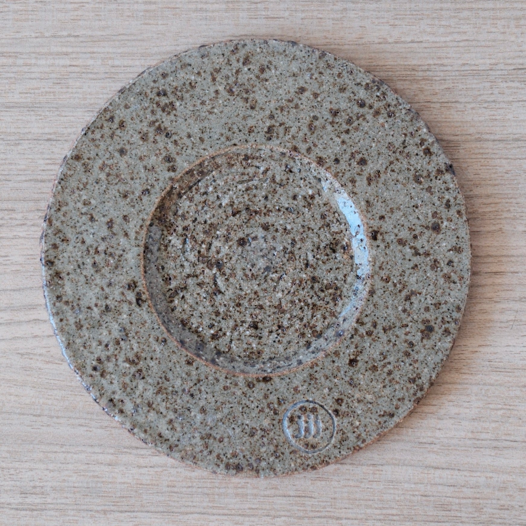 Round ceramic coaster with olive speckled pattern on a wooden surface
