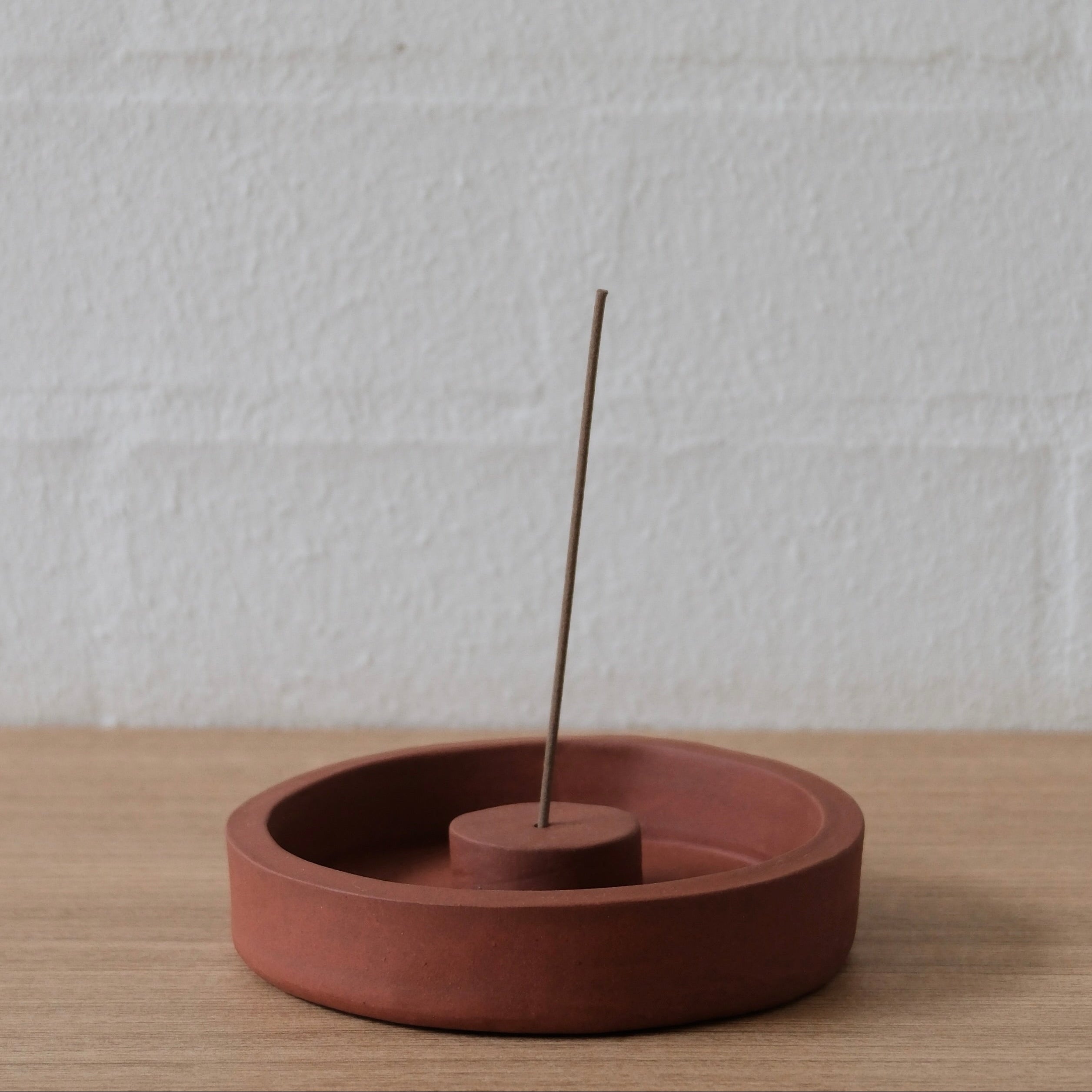 Terracotta incense burner with a single incense stick on a light wooden surface and white textured background
