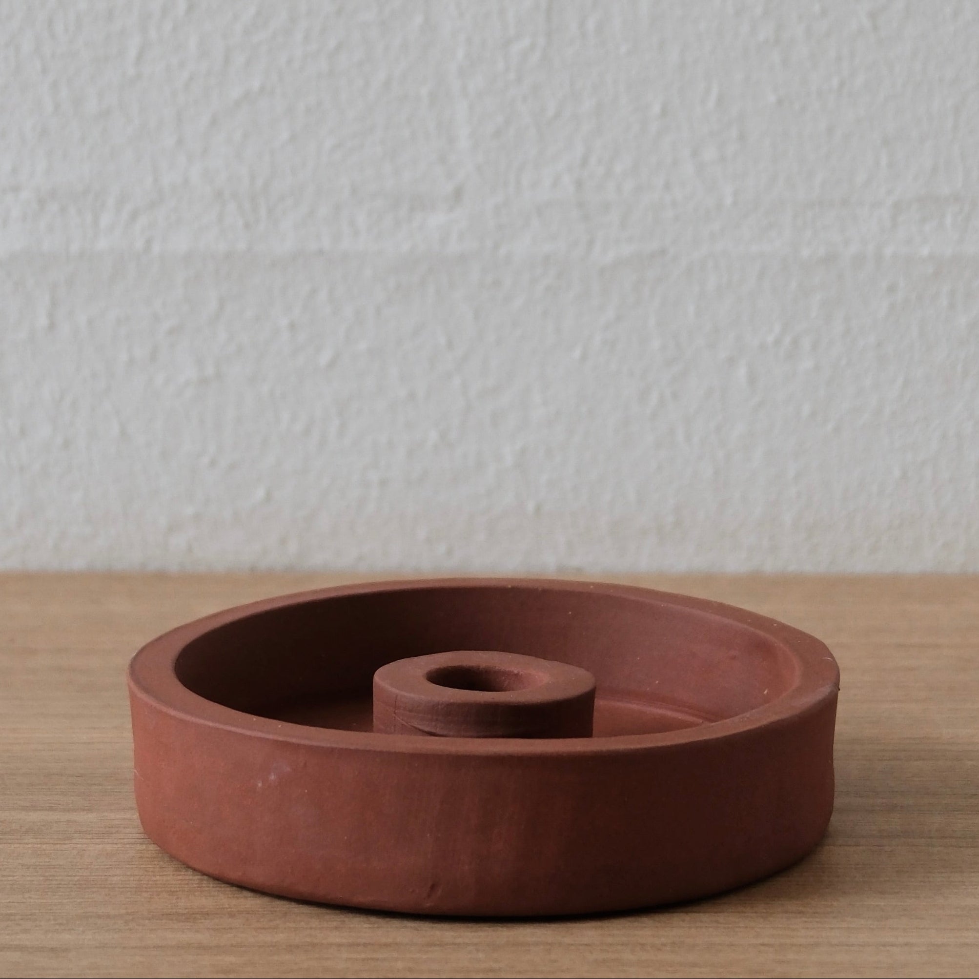 Terracotta candle holder on a wooden surface with a white textured background