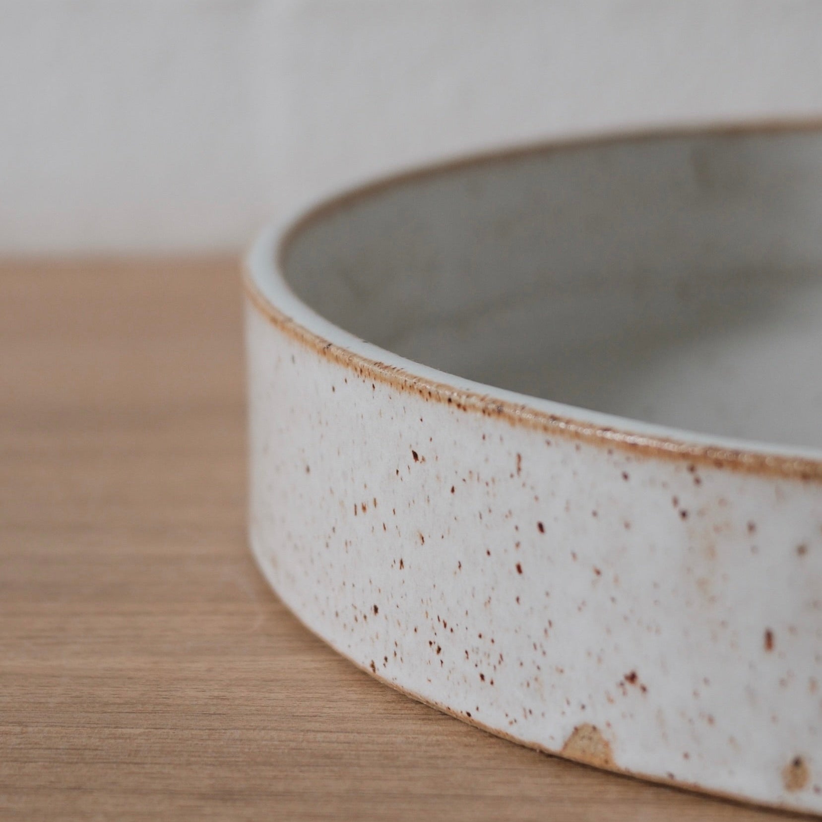 Close-up of the straight side of a white ceramic dish with a slightly speckled finish on a wooden surface.