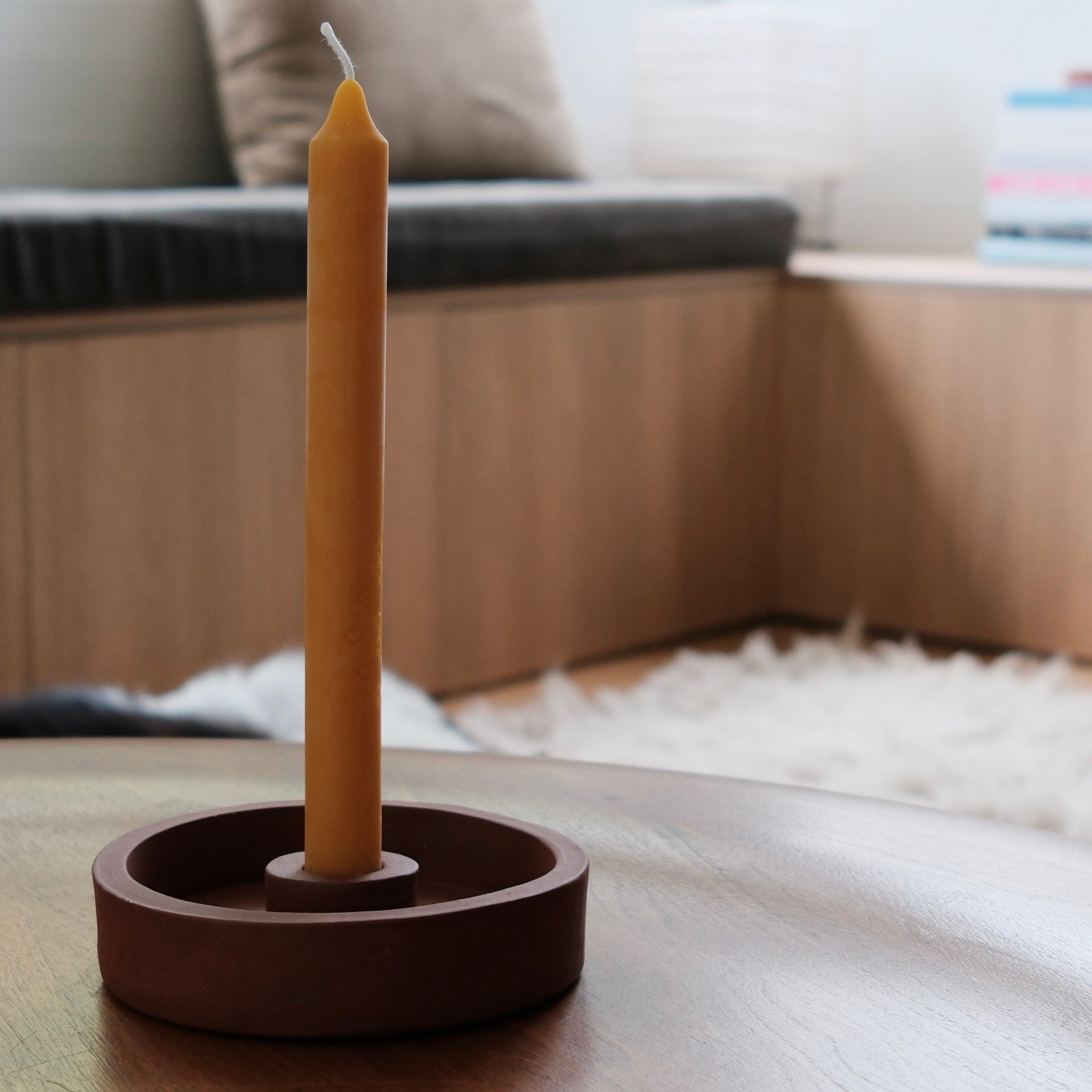 Golden candle in a terracotta candle holder on a wooden side table with a blurred background