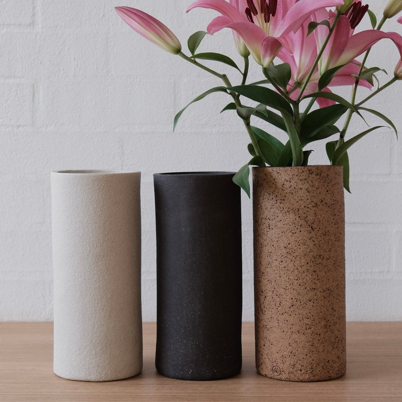 A trio of tall cylindrical vases, in matte white, dark charcoal and speckled warm brown finishes