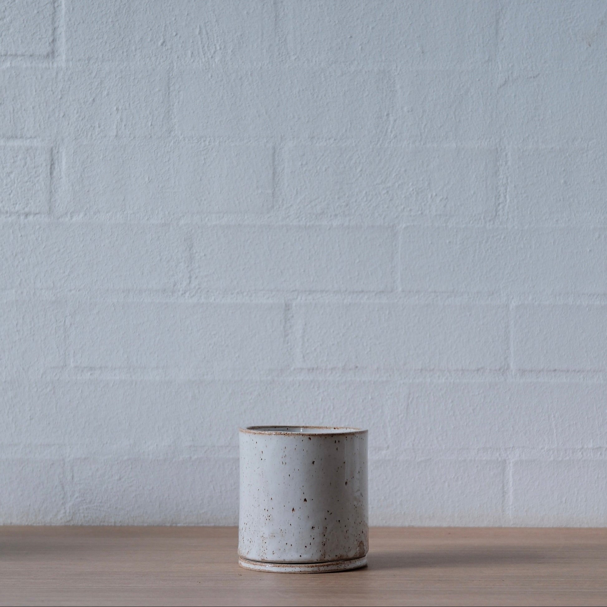 Small speckled warm white ceramic planter on a wooden surface with a white brick wall background