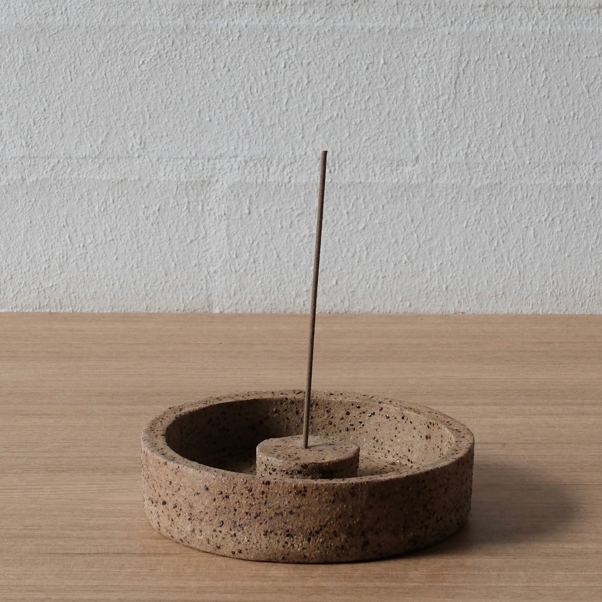 Ceramic incense burner with warm brown speckled finish with a single incense stick on a wooden surface.