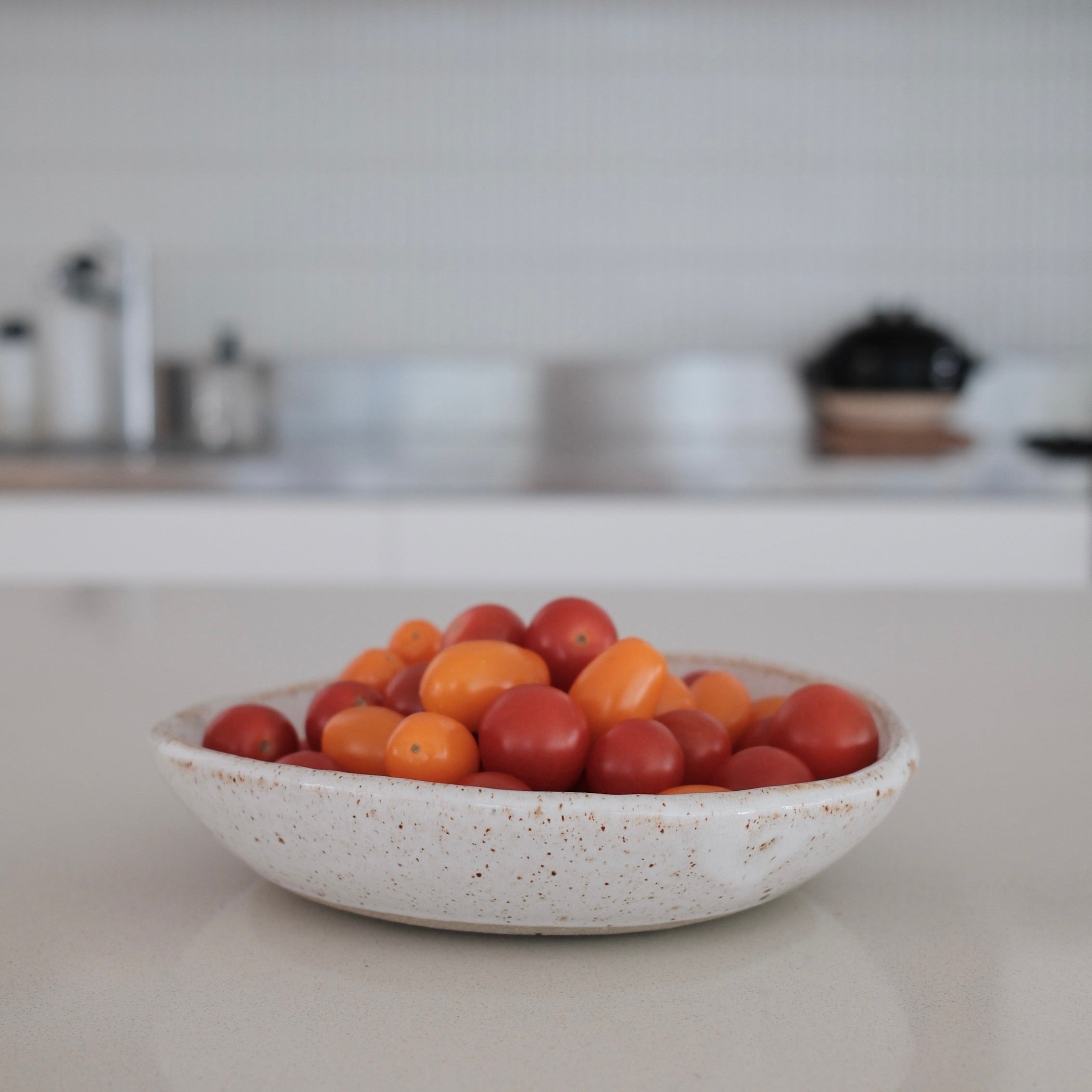 Ceramic bowl of tomatoes on a kitchen counter with a blurred background