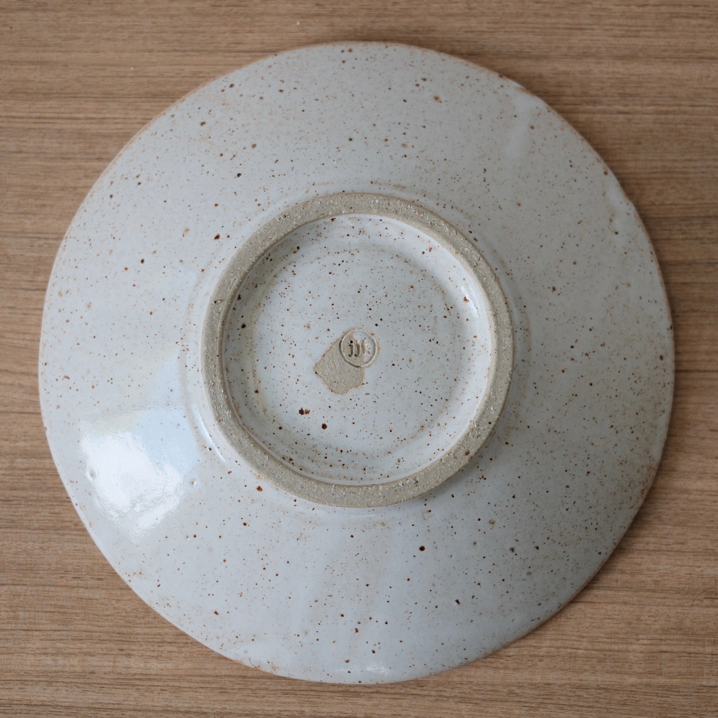 Underside of ceramic bowl with foot and makers mark on a wooden surface
