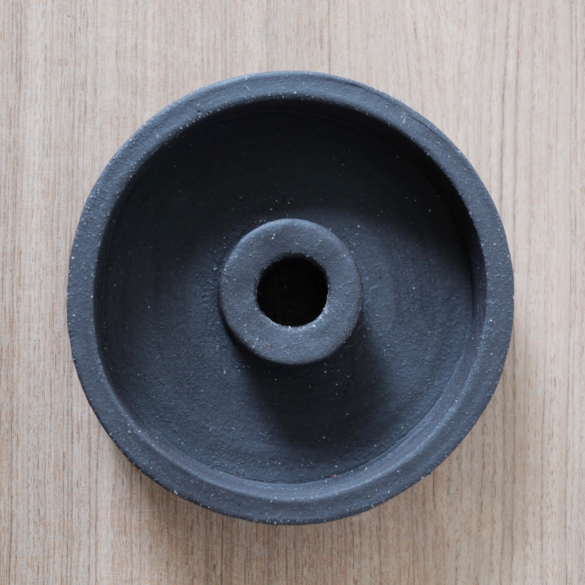 Birds-eye-view of a black ceramic candle holder on a light wood surface