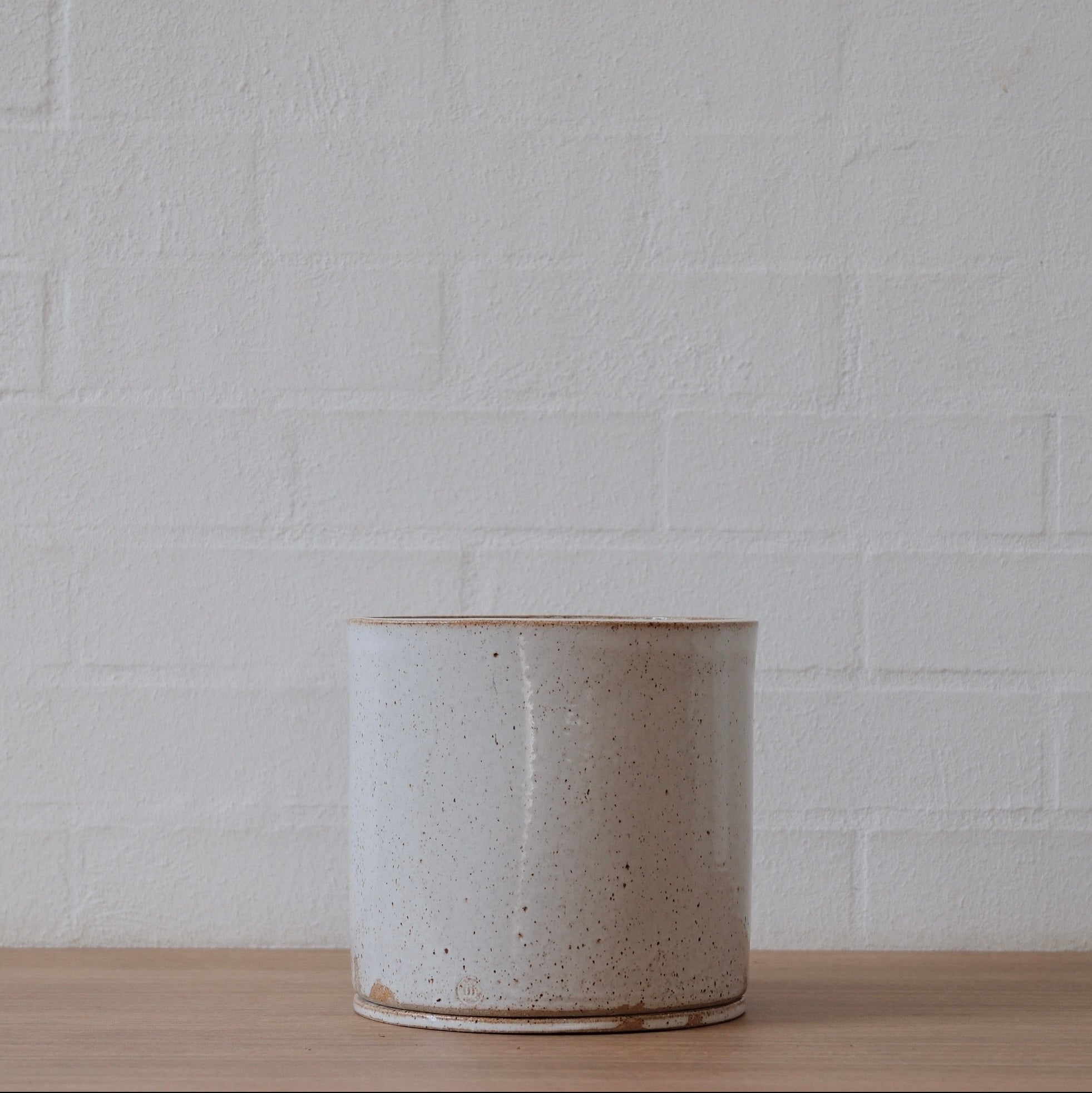 Large speckled warm white ceramic planter on a wooden surface with a white brick wall background