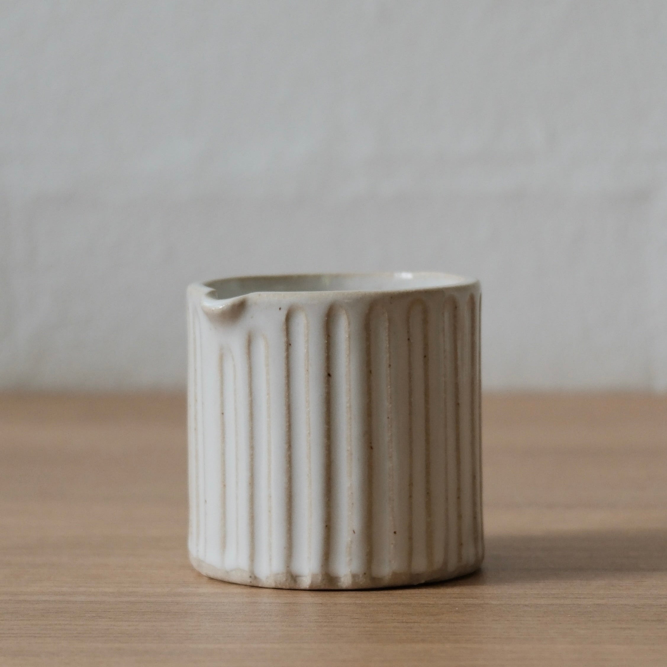 White ceramic jug with ribbed texture on a wooden surface and white background