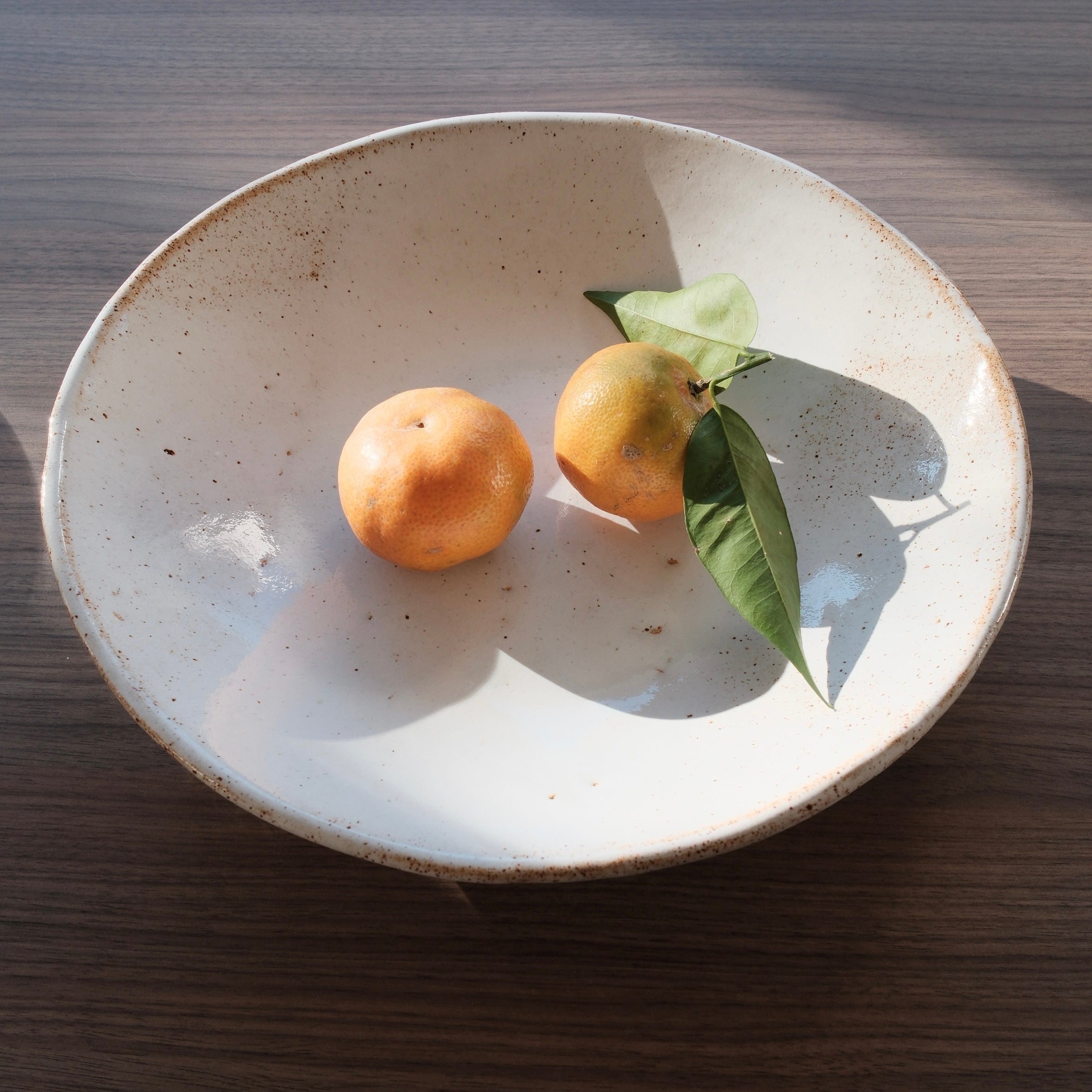 Two oranges with a leaf on a ceramic platter on a wooden table
