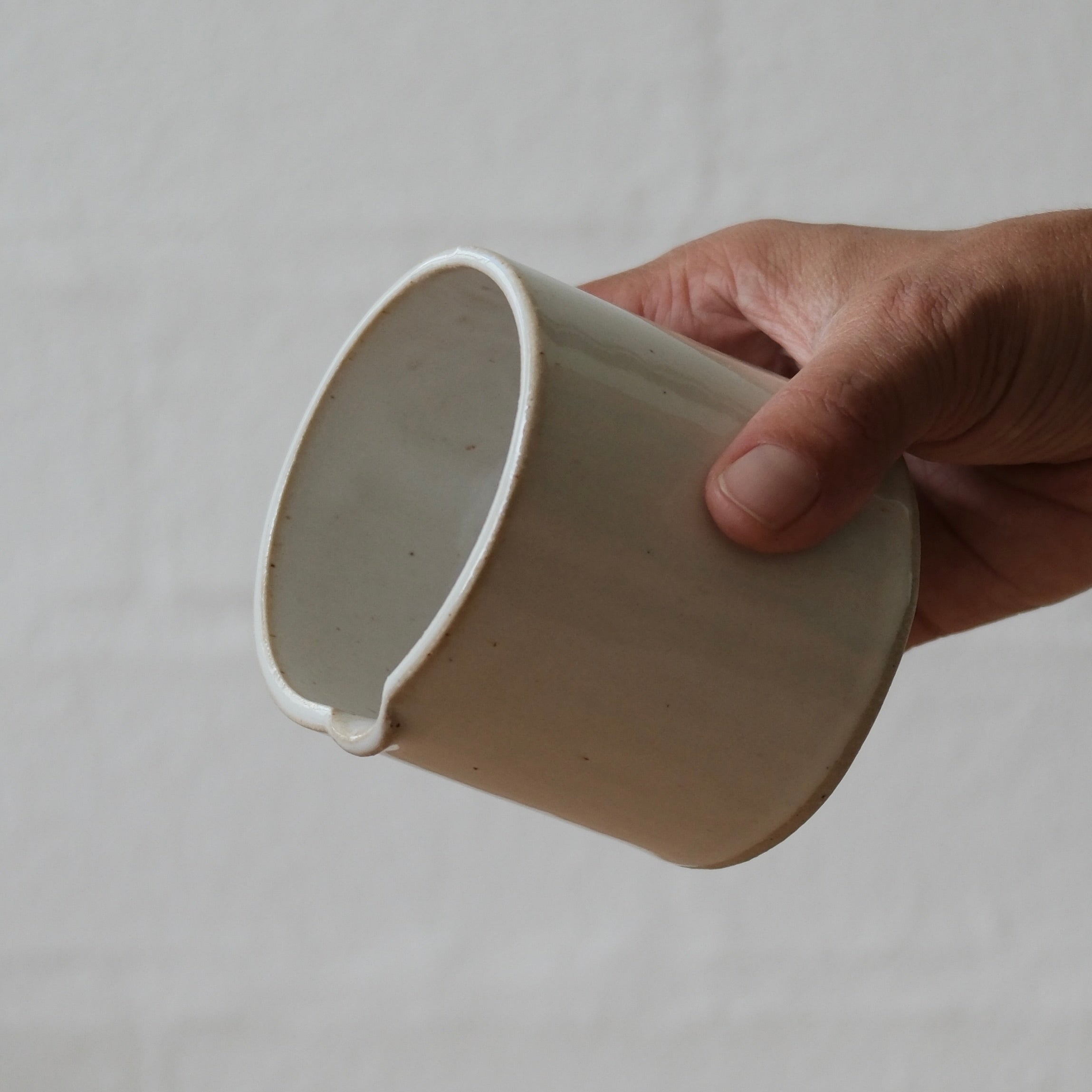 Hand holding a small white ceramic jug against a plain background