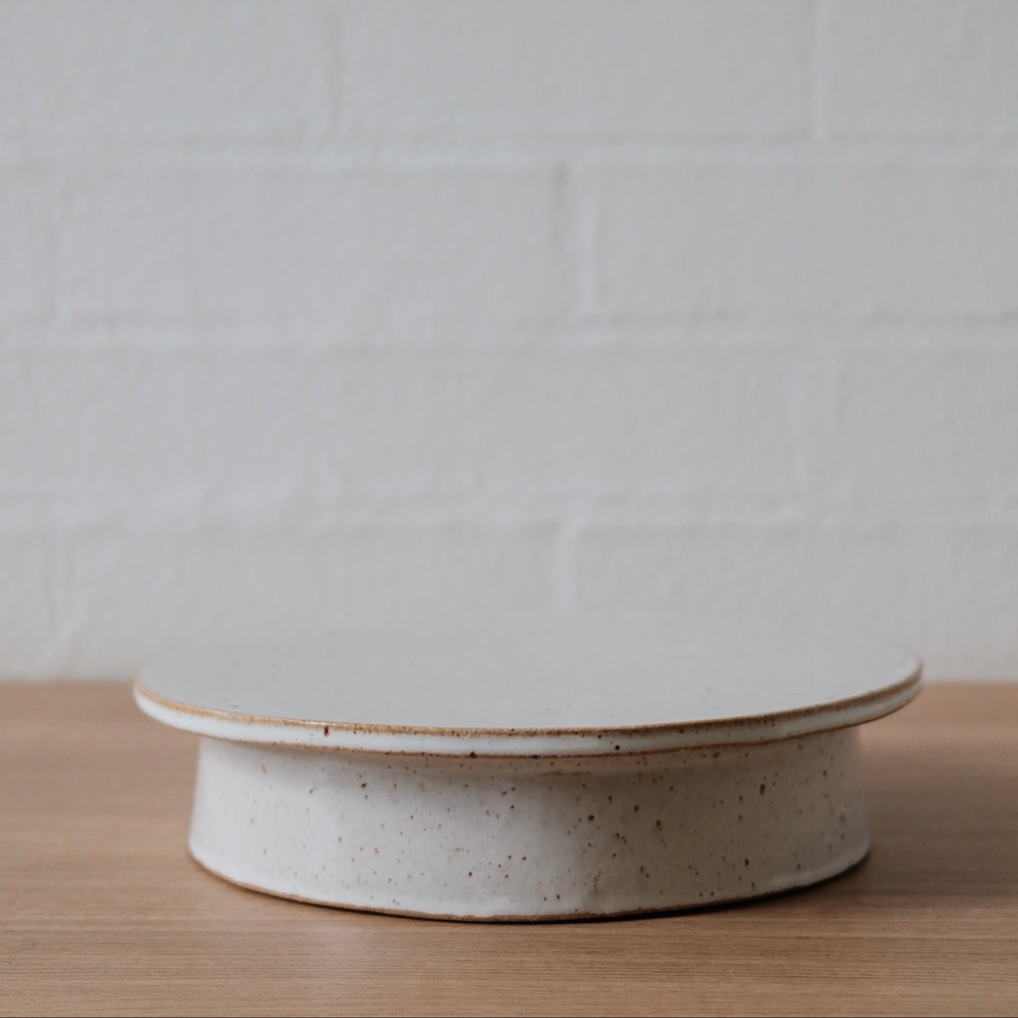 White speckled ceramic cake stand on a wooden surface with a white background