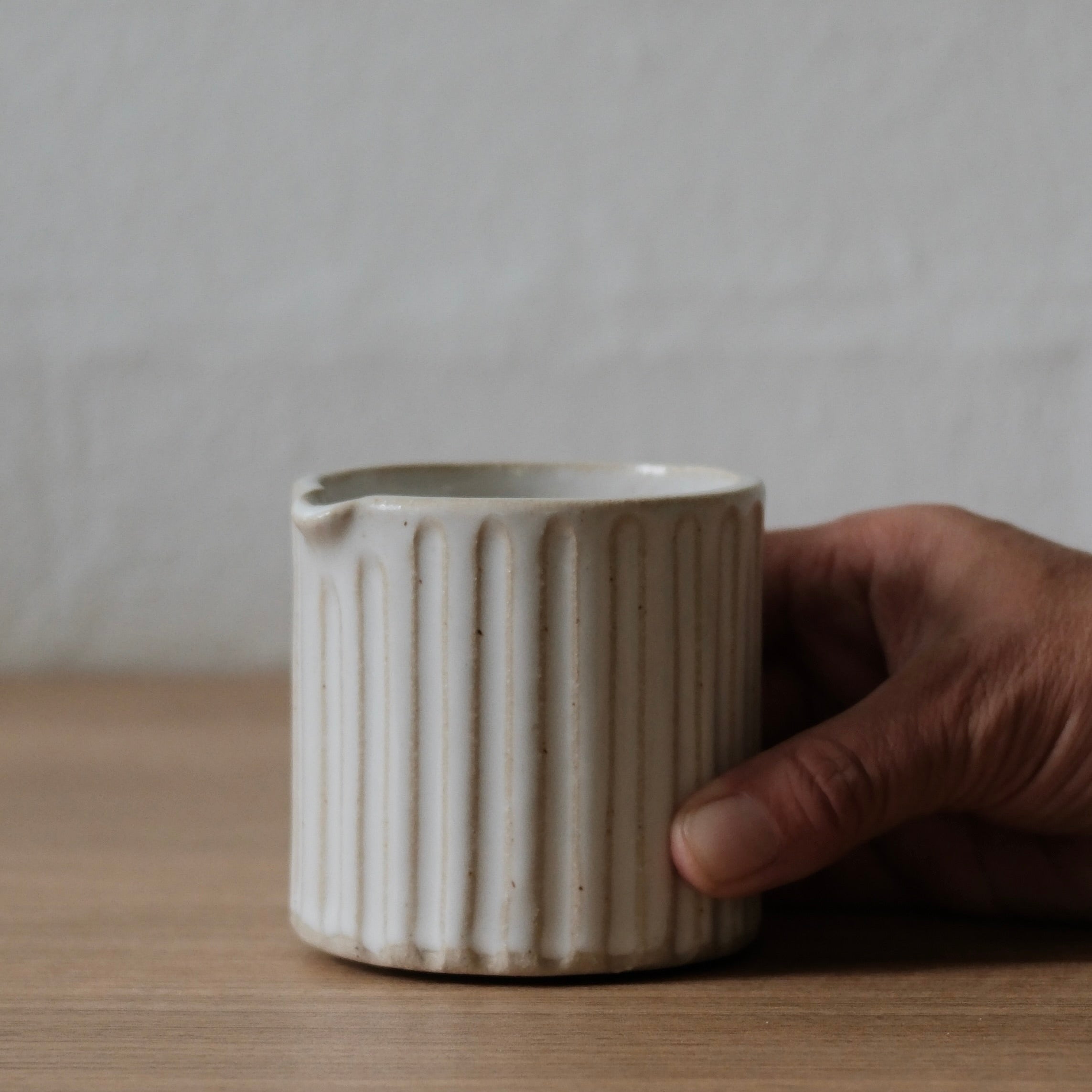 Hand holding a small white textured ceramic jug against a neutral background