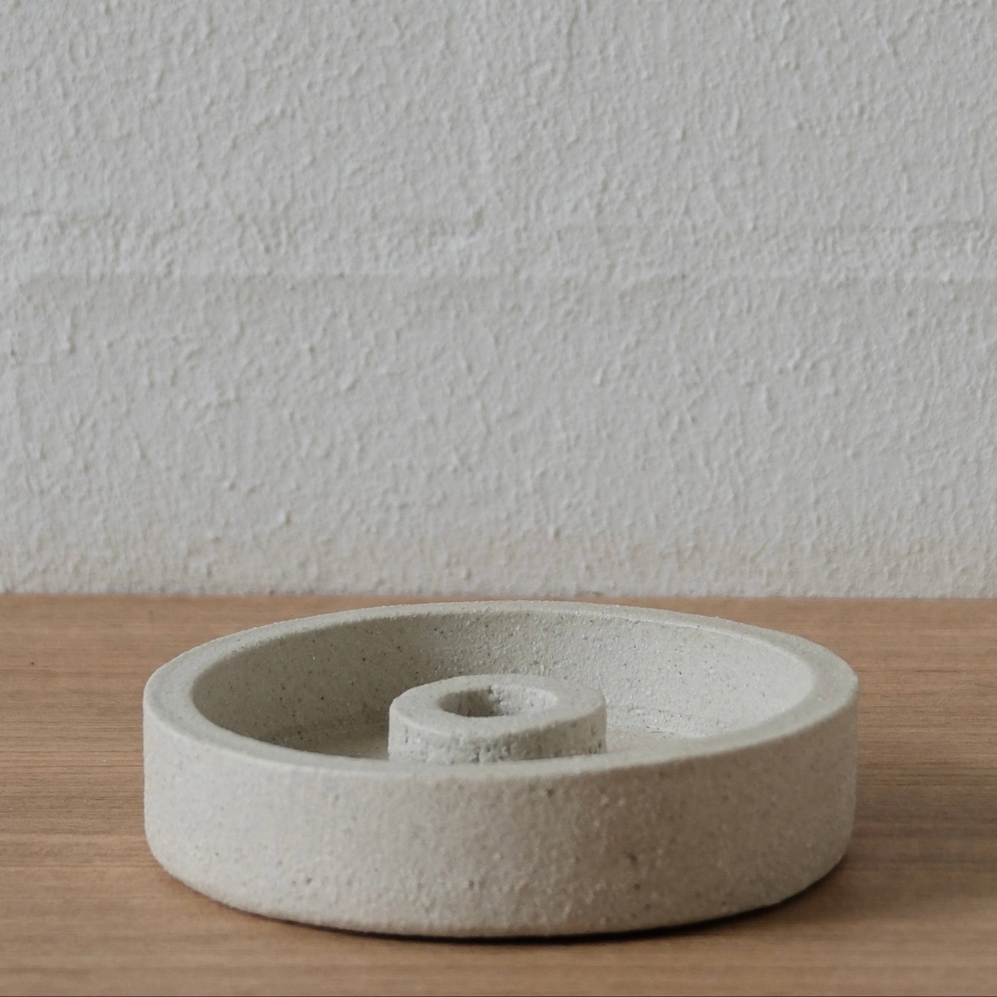 White textured ceramic candle holder on a wooden surface with white background