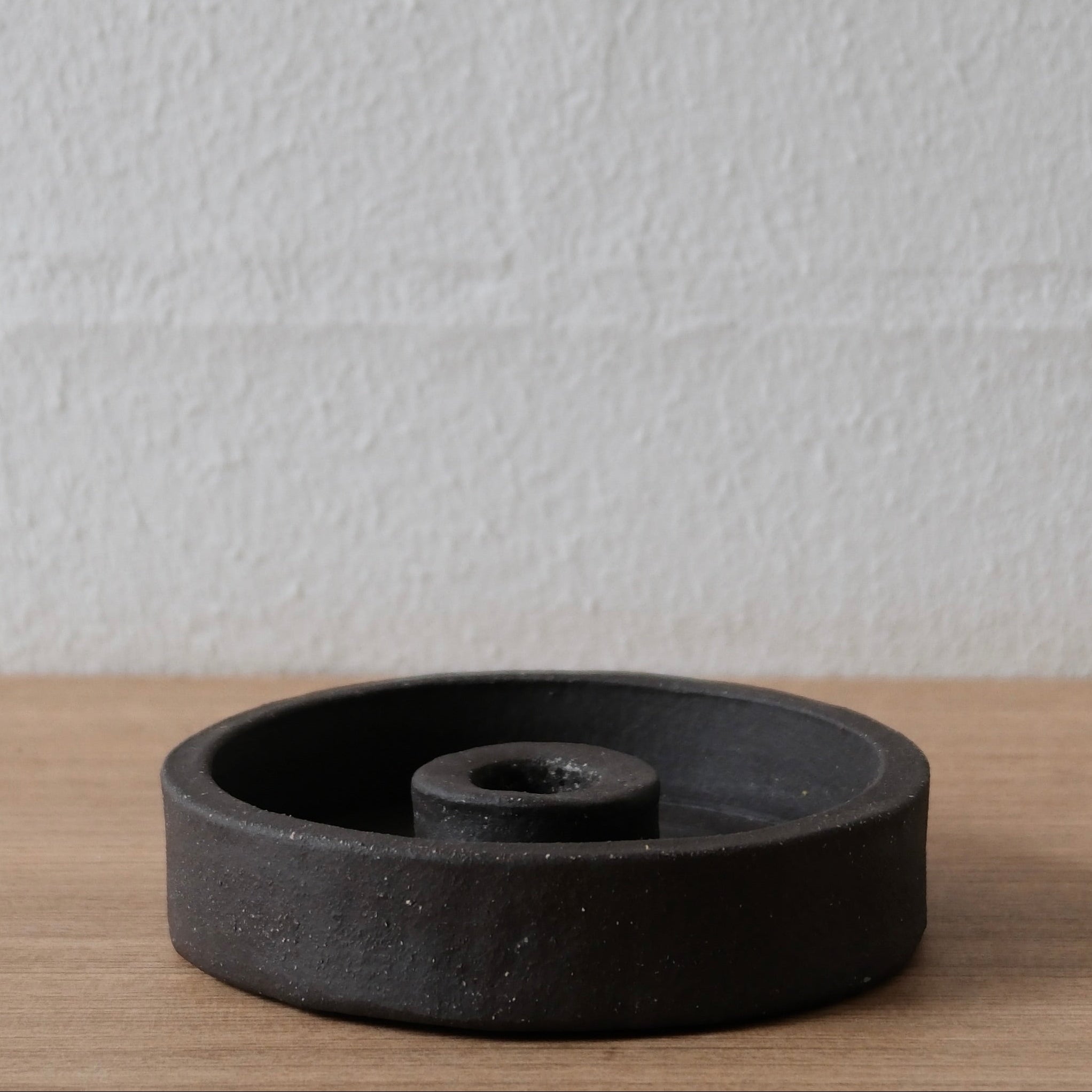 Black ceramic candle holder on a wooden surface with a white background