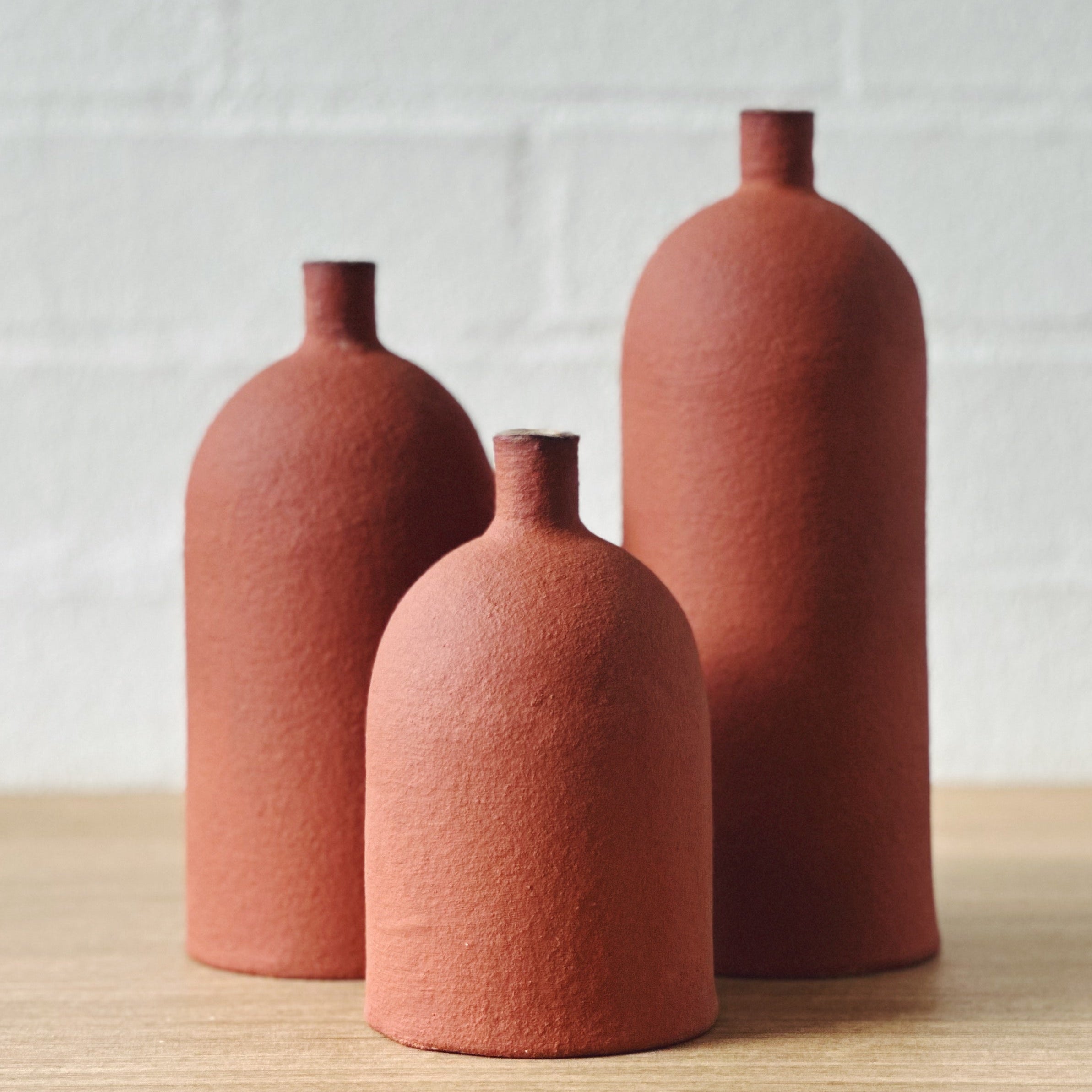 Three terracotta ceramic vases in various sizes, all with cylindrical body and dome top, placed against a white backgroud
