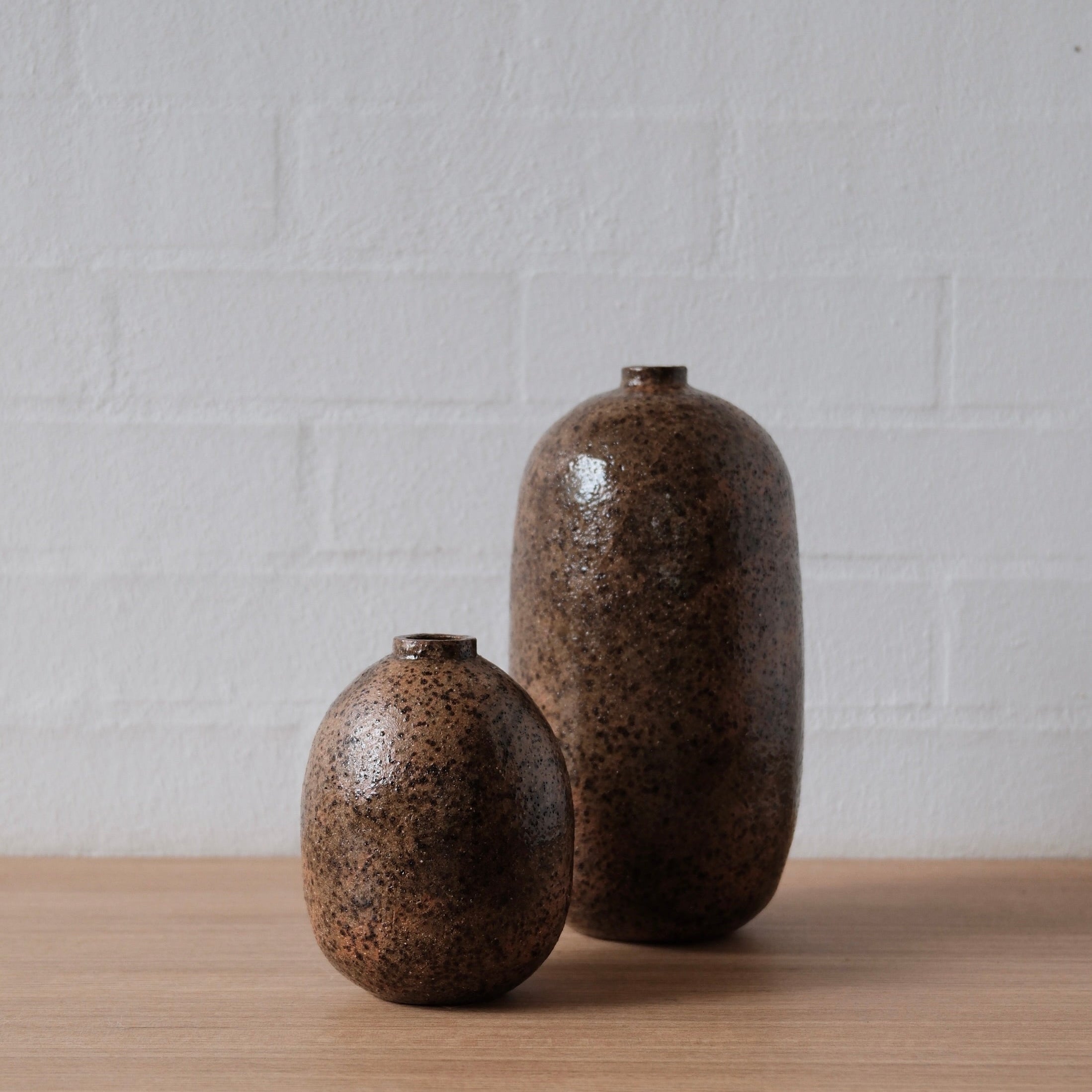 Two brown ceramic vessels on a wooden surface with a white brick wall background