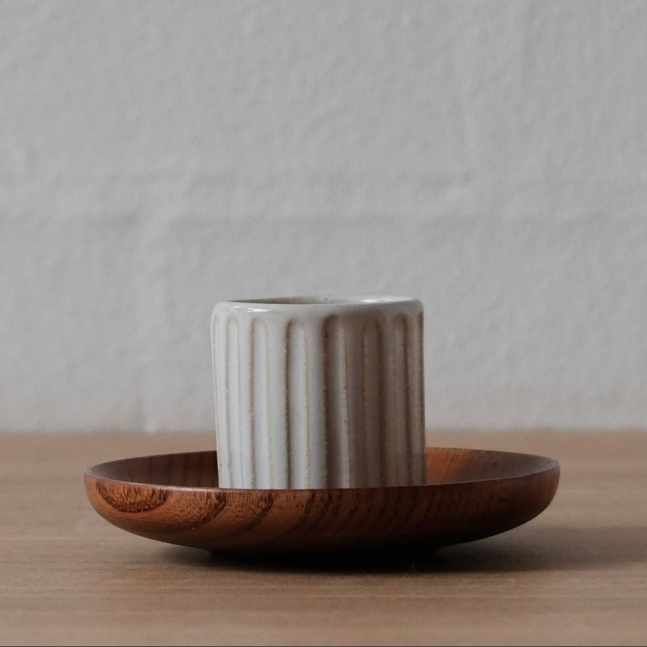 Ceramic espresso cup with ribbed texture on a wooden saucer against a neutral background