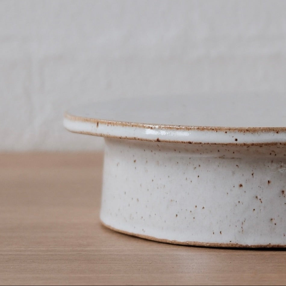 Close up of white speckled ceramic cake stand on a wooden surface with a white background