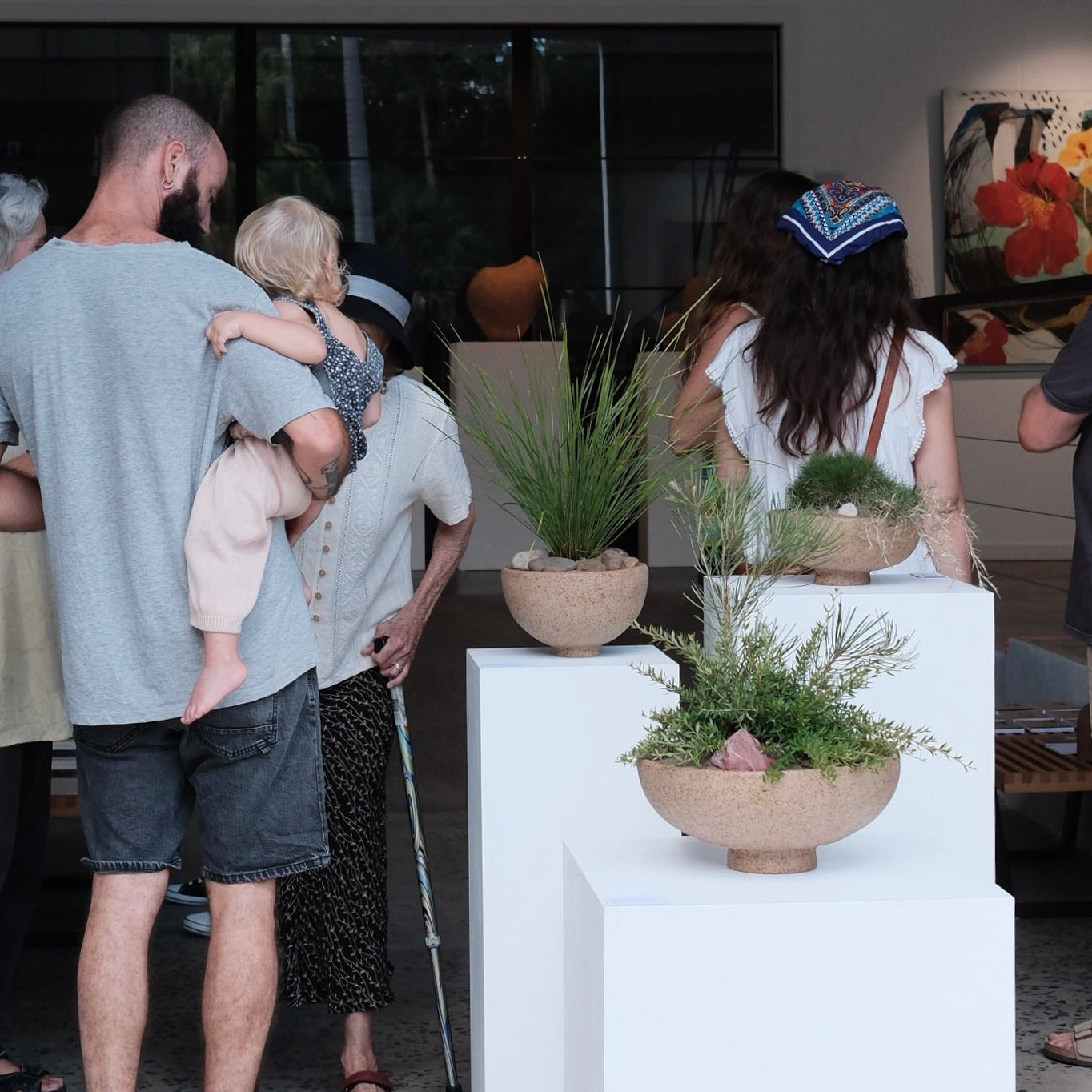People gathered around a display of plants and artwork inside a building.