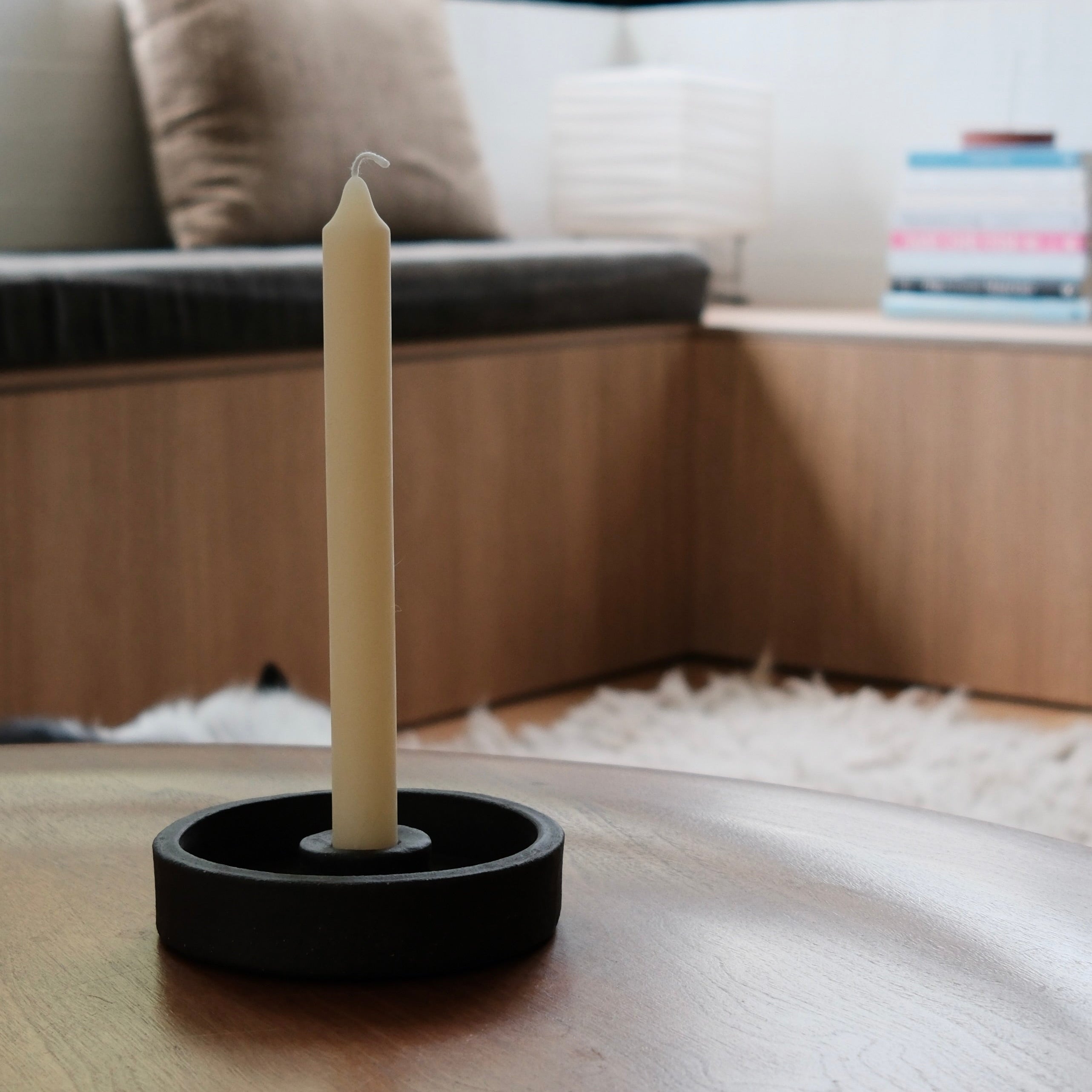 Candle in a black ceramic candle holder on a wooden surface with a blurred indoor background
