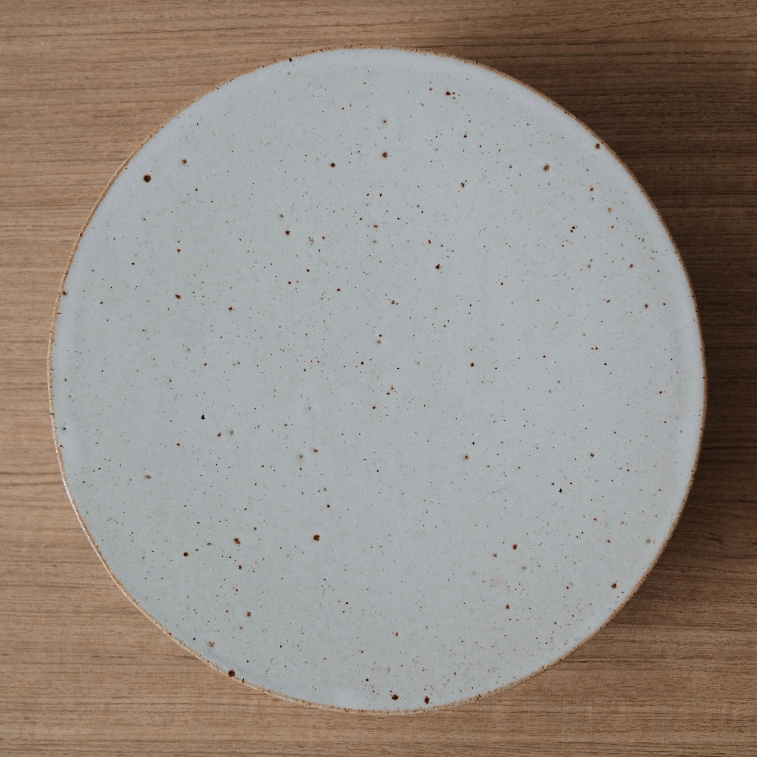 Top down view of round ceramic cake stand with speckled texture on a wooden surface