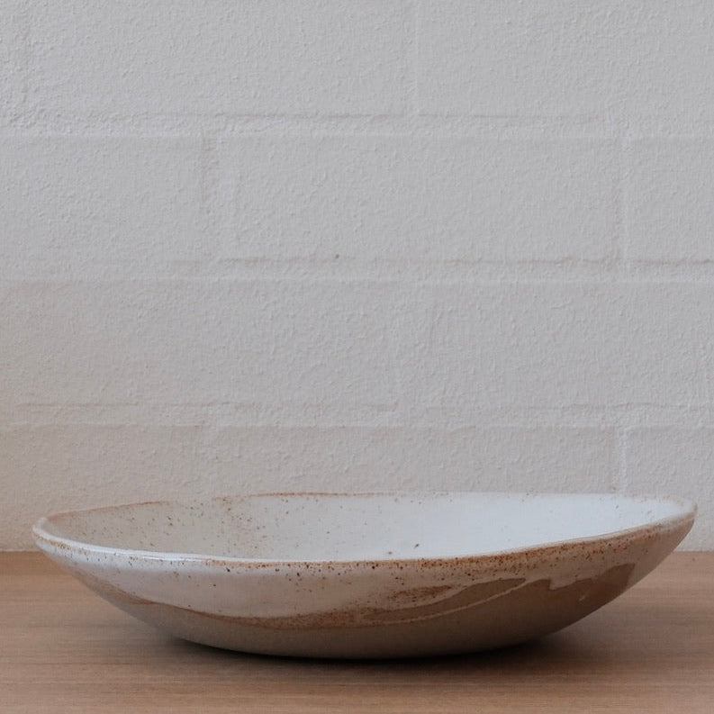 Ceramic platter bowl on a wooden surface with a white textured wall background