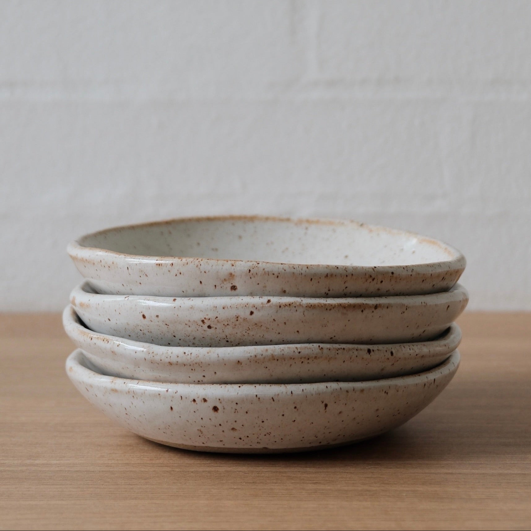 Stack of four white ceramic bowls on a wooden surface with a white background