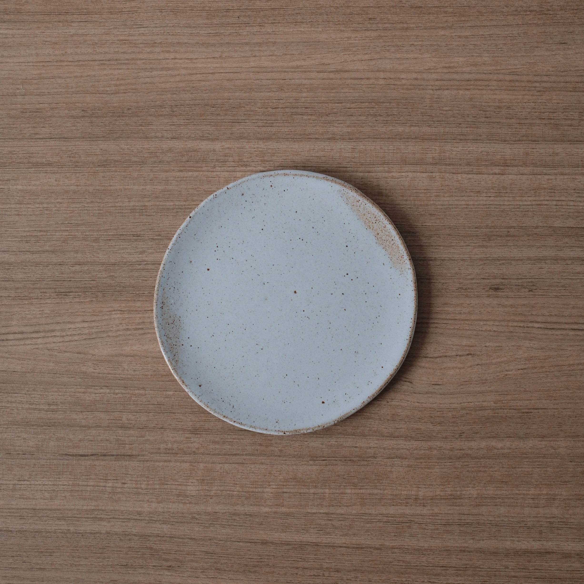 Round white ceramic side plate with a slightly speckled finish and golden highlights on a wooden surface