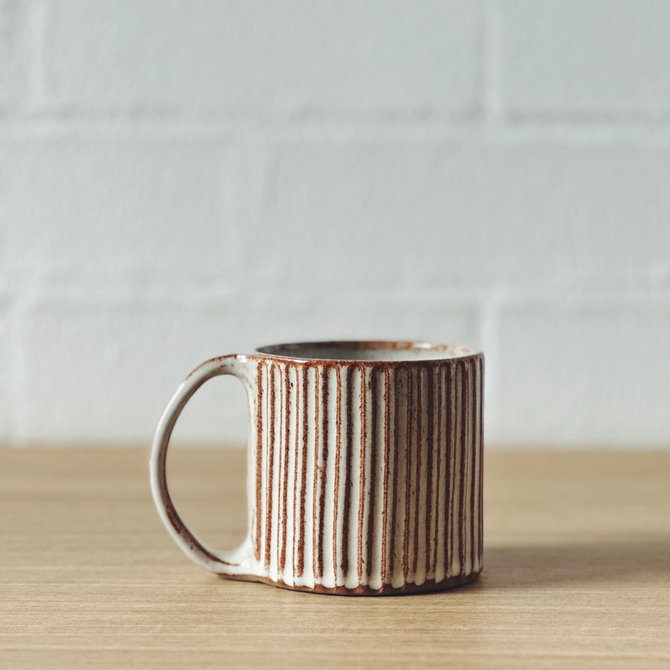 A handcrafted ceramic mug with a striped pattern and a warm beige and brown colour scheme, displayed against a white background.